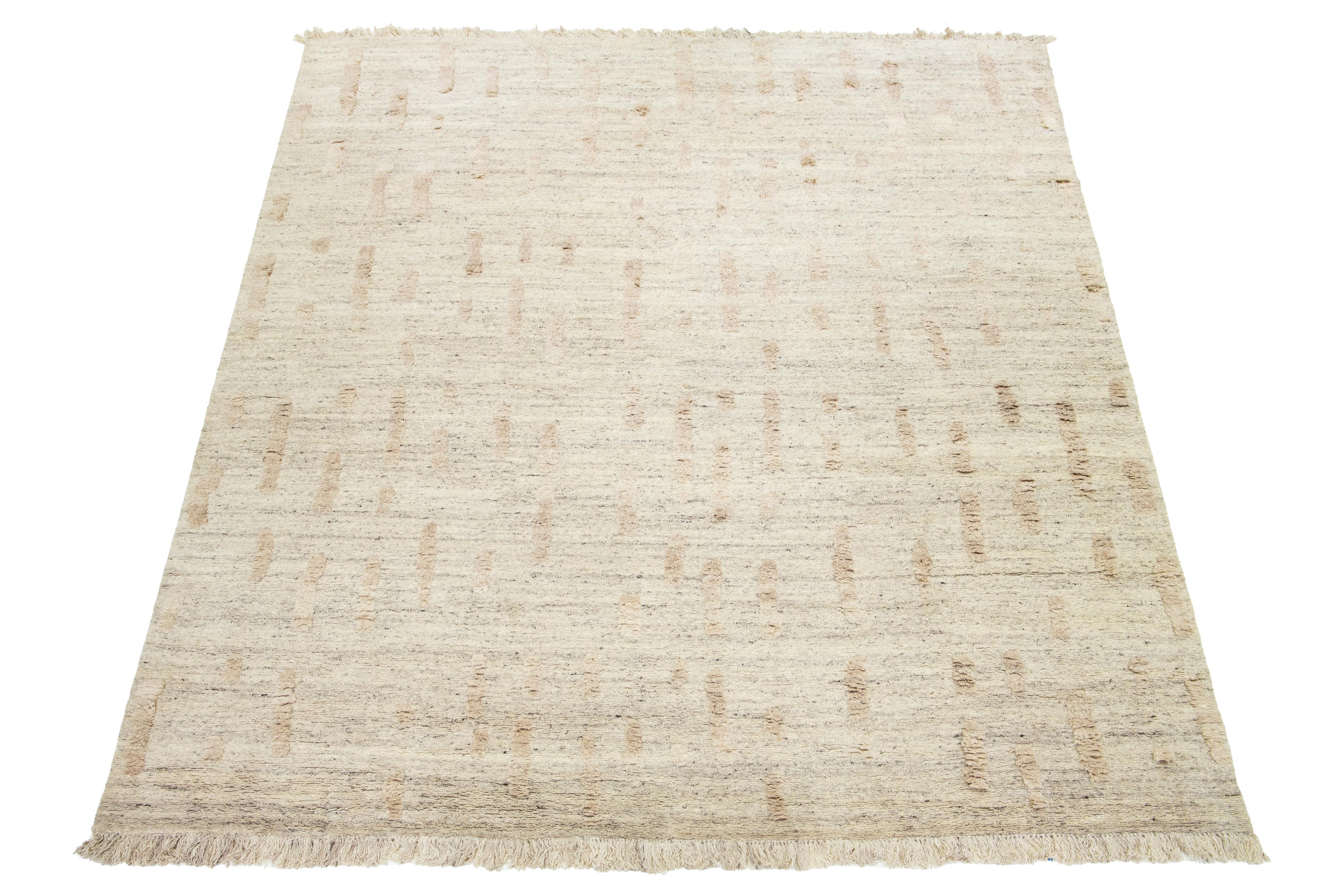 This hand-knotted organic Moroccan wool rug features a beige background with geometric designs and fringes. It serves as a stunning centerpiece for any room.

This rug measures 12' x 14'11