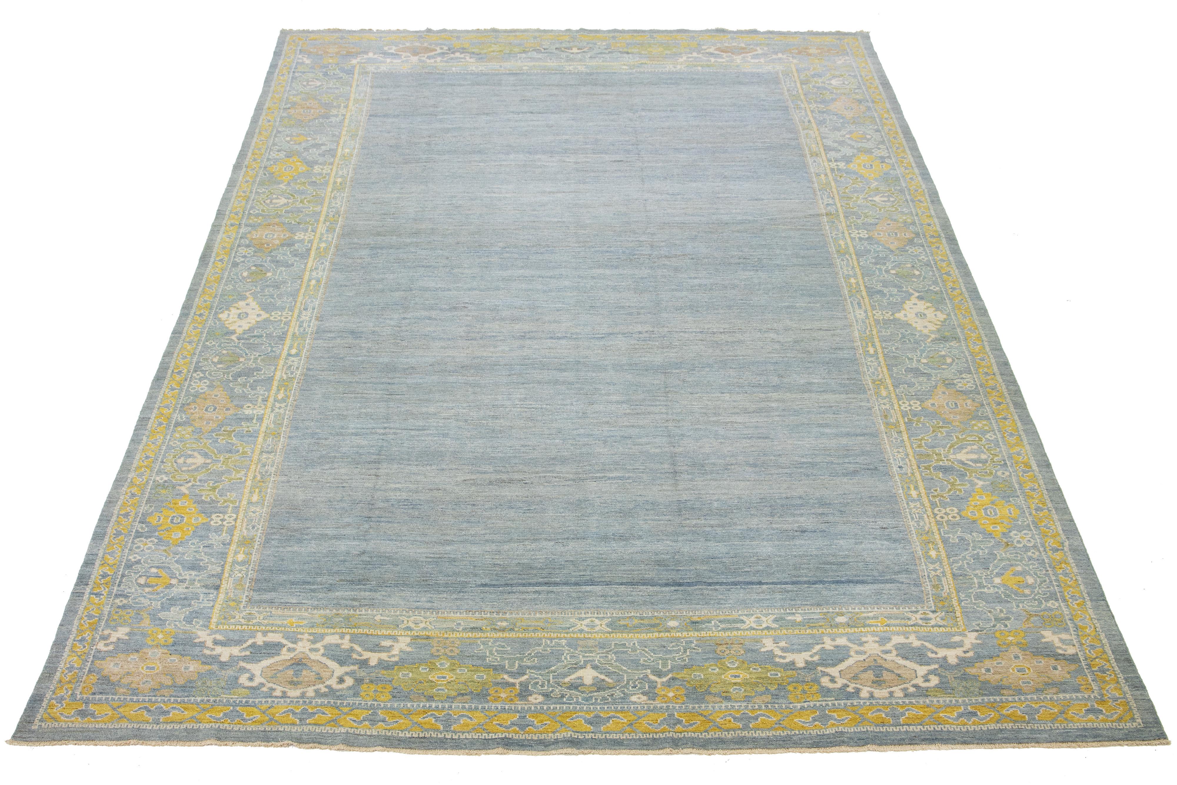 Ce tapis en laine noué à la main présente un fond bleu clair avec des accents jaunes et beiges dans un motif encadré.

Ce tapis mesure 11'11'' x 18'7''.