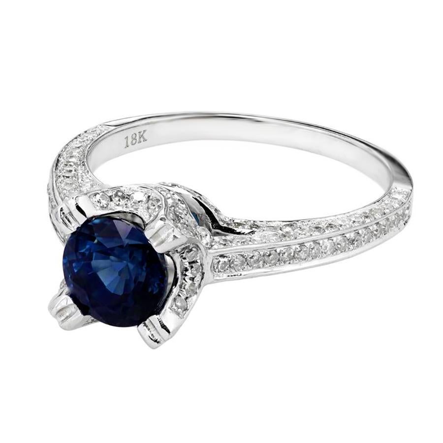 Sapphire and Micro Pavé diamond 18k white gold engagement ring. The round-shaped 1.20ct sapphire gemstone is mounted in a 18k white gold setting with a halo of round cut micro pave diamonds, which also run along the top, shoulders and bottom of the