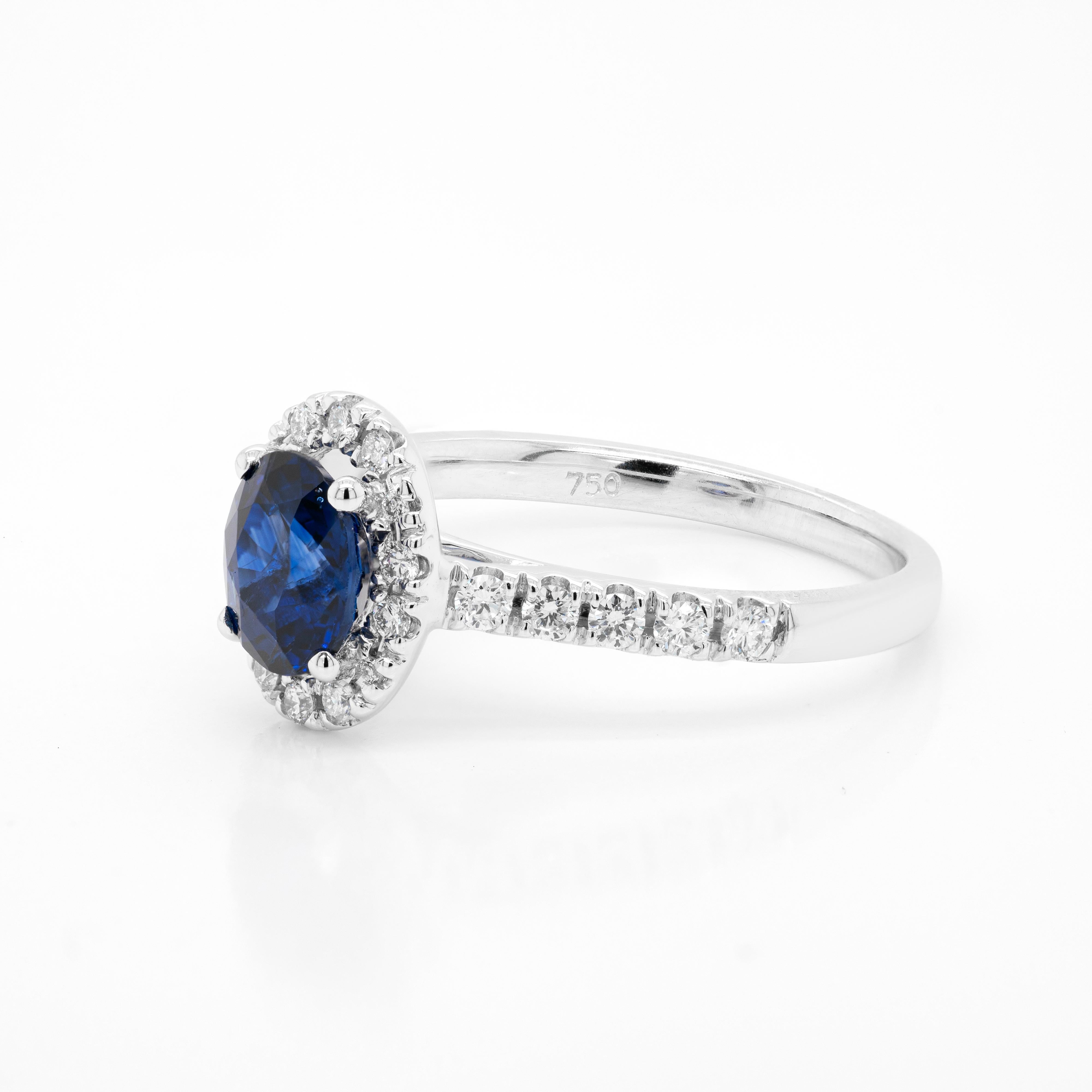 This wonderful engagement ring features a beautiful oval blue sapphire weighing 1.20ct, mounted in a four claw, open back setting. The vibrant stone is surrounded by a halo of 14 round brilliant cut diamonds sat atop a delicate diamond set shank