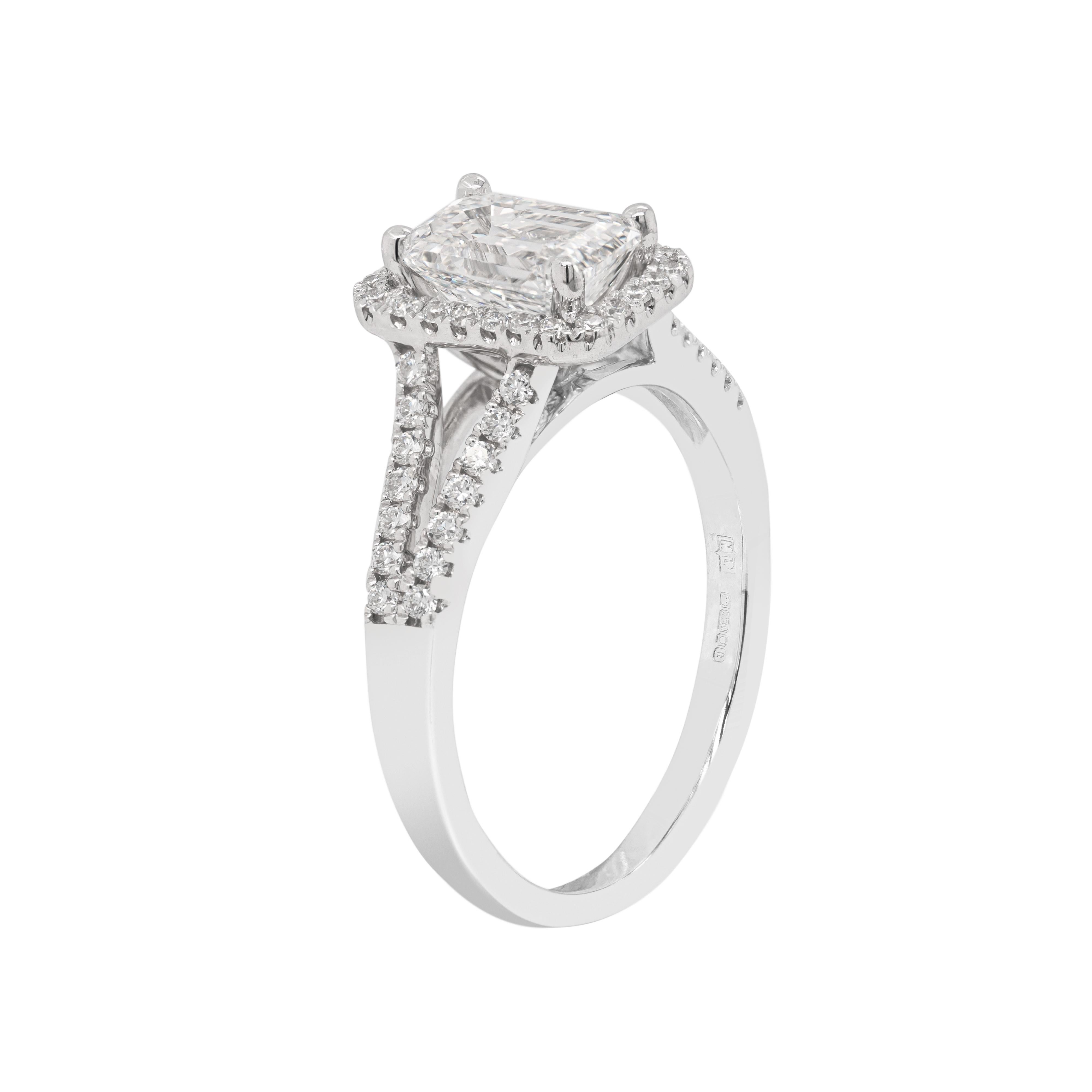 This elegant engagement ring features a GIA certified 1.20 carat emerald cut diamond, graded H, SI2. The gorgeous stone is beautifully surrounded by a halo of round brilliant cut diamonds sat atop a diamond set split shank making the total diamond