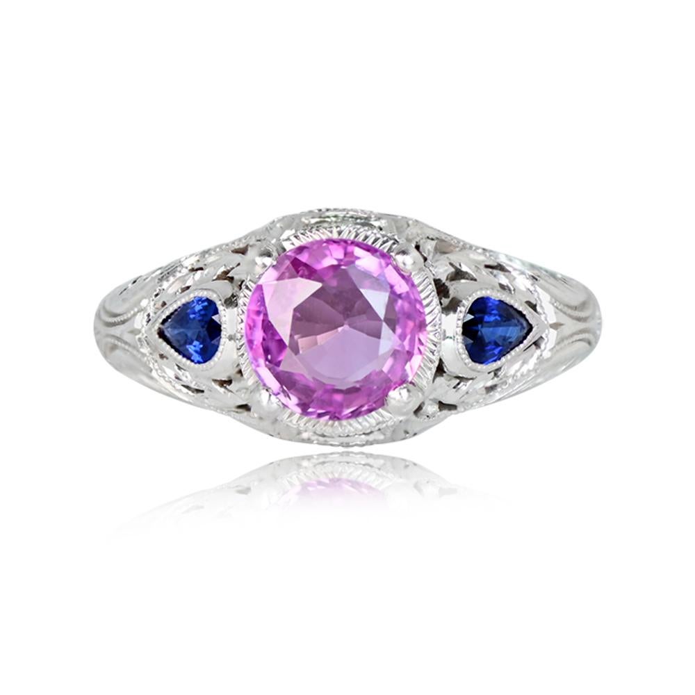 Captivate with this exquisite platinum ring featuring a central round-cut pink sapphire, approximately 1.20 carats, delicately set in prongs. The shoulders boast pear-shaped accent sapphires in bezel settings, surrounded by open-work details adorned