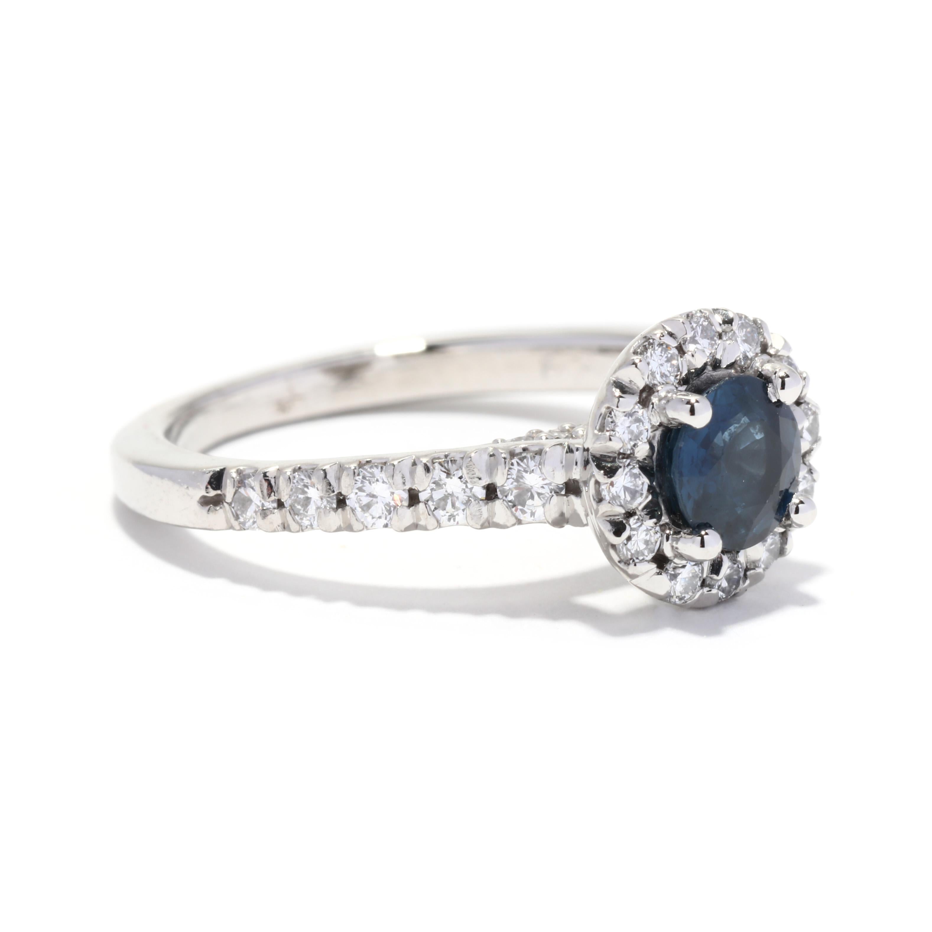 A vintage platinum sapphire and diamond halo engagement ring. This alternative engagement ring features a prong set, round cut sapphire weighing approximately .70 carat surrounded by a halo of full cut diamonds and with diamonds down the band and on