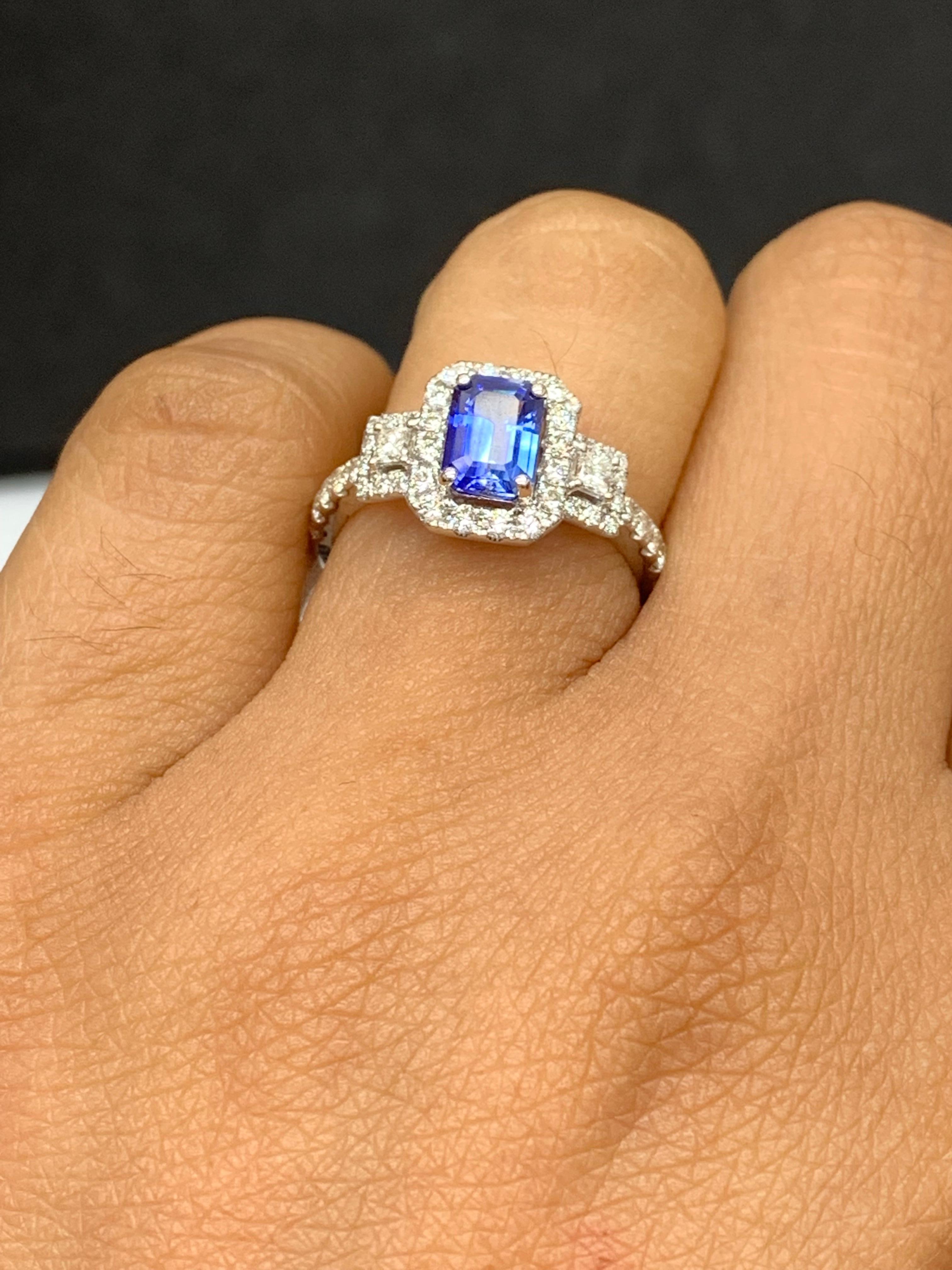 A stunning ring showcasing a rich emerald cut Blue Sapphire weighing 1.21 carats surrounded by diamonds. The center stone is surrounded by a row of 42 diamonds, weighing 0.57 carats total, with 2 princesses cut diamonds on each side weighing 0.12