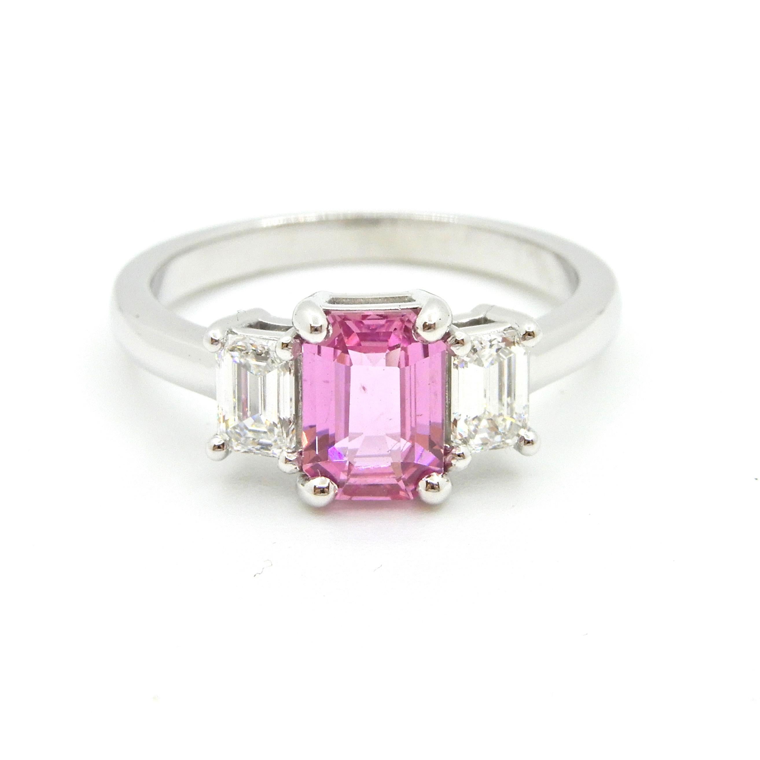 This 1.21 Carat Emerald Cut Pink Sapphire and Diamond Engagement Ring is set in 18 carat white gold. The rounded band flows up to support a central 4 claw mount holding an emerald cut natural, no heat pink sapphire with 4 claw set emerald cut