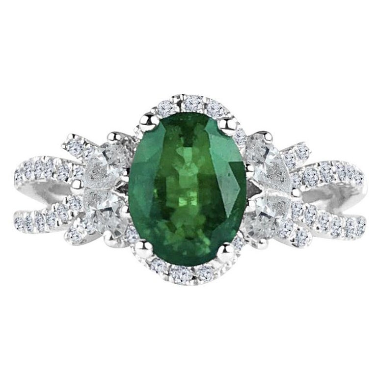 This ring features a deep green 1.21 carat oval cut fine emerald center, flanked by four pear shaped diamonds and additional round diamond halo, and round diamonds tracing down the split shank. From the side, the diamonds give the impression of a