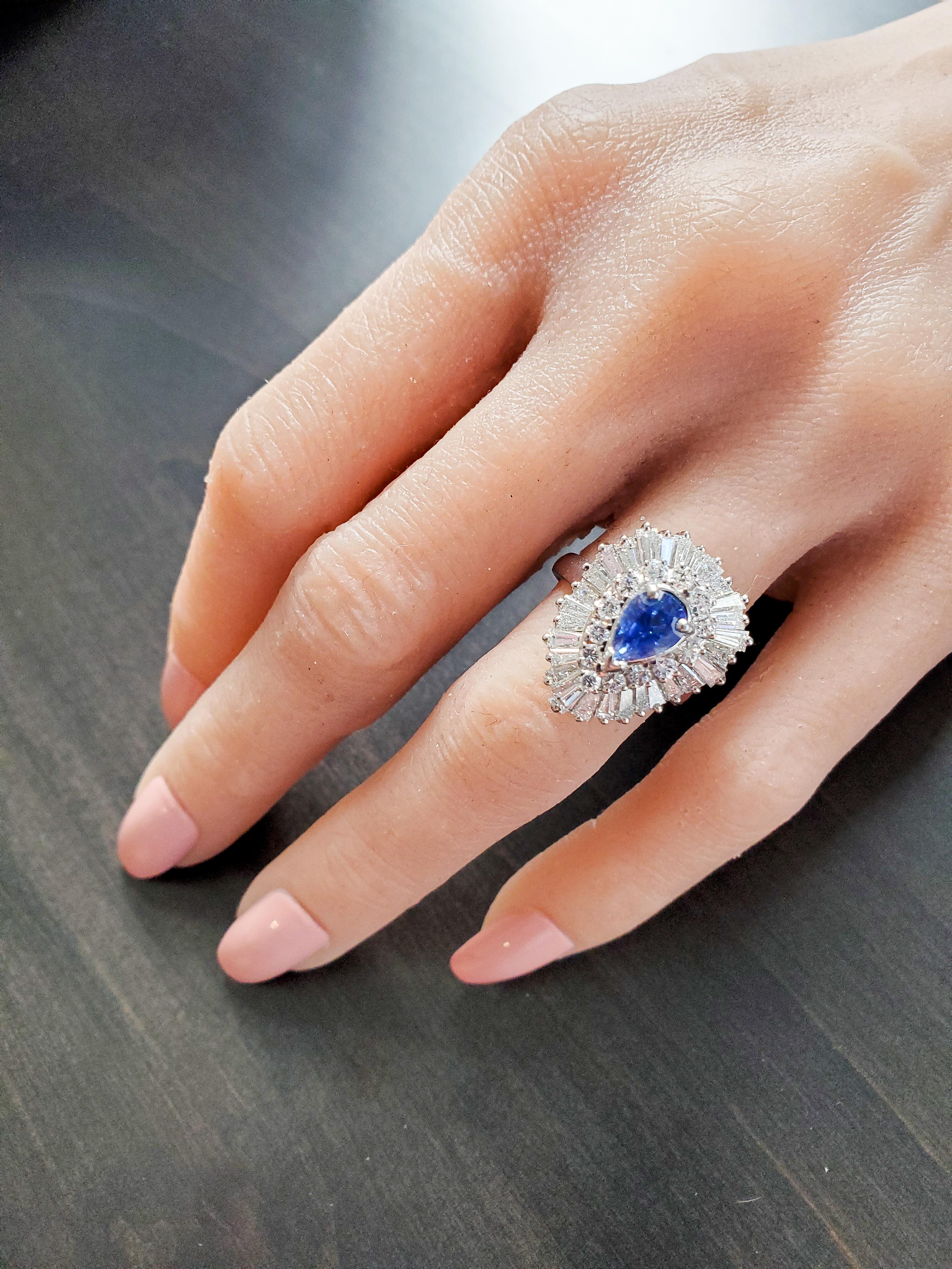 Custom made in luscious platinum with a bright polished finish, this extraordinary cocktail ring features a pear-shaped fine blue sapphire prong set in the center with a weight of 1.21 carats. Sparkling round brilliant cut and shimmering baguette