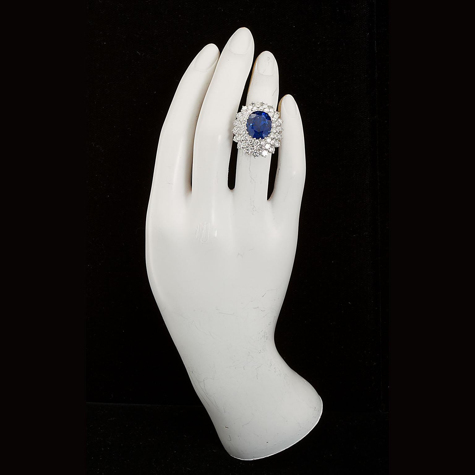 A Burmese Unheated deep transparent blue oval sapphire and diamond cluster ring.  Centering on an Oval shape 12.10 carat blue sapphire set in a round brilliant-cut diamond surround; estimated total diamond weight 5.25 carats; mounted in