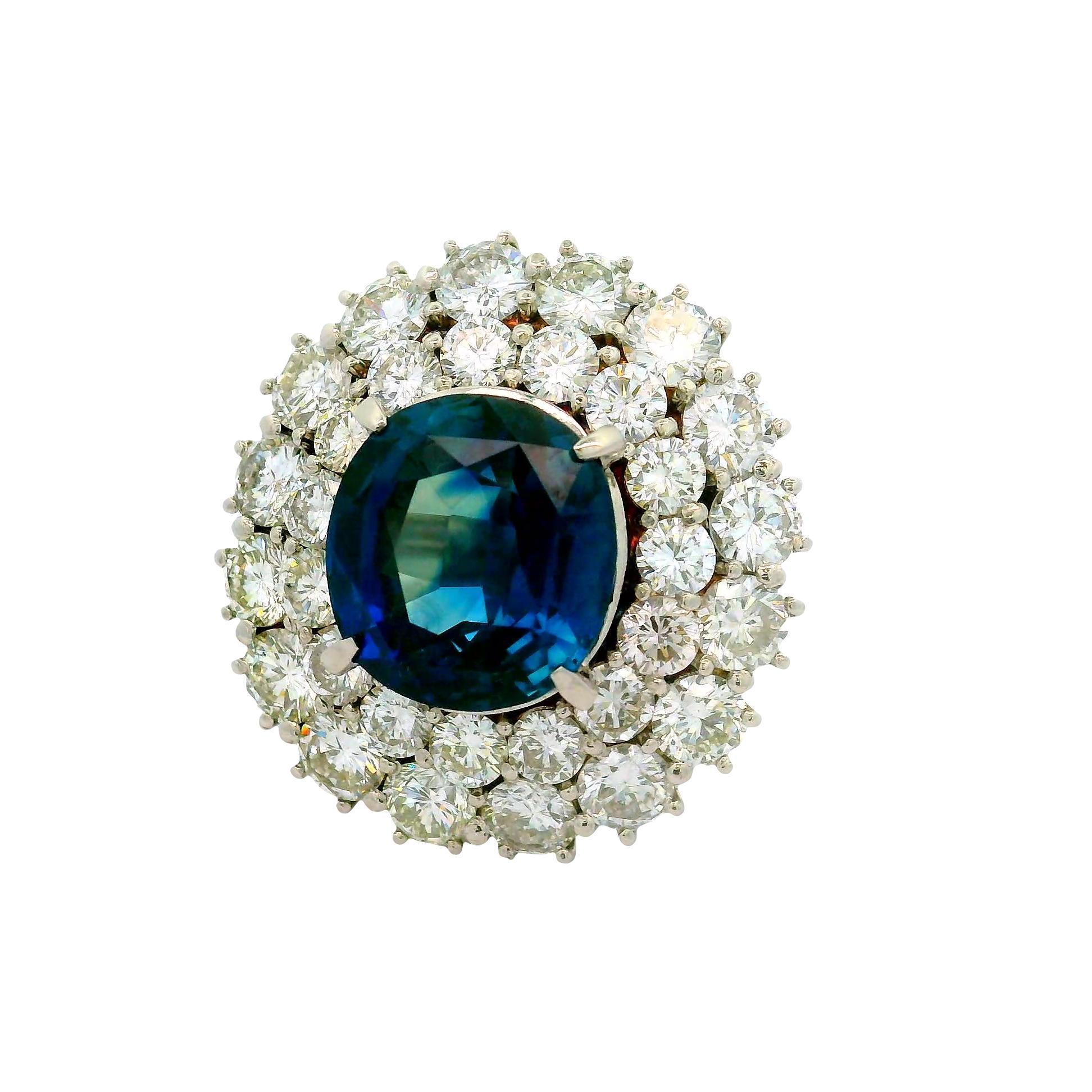 An exquisite oval-cut sapphire, weighing 12.13 carats, takes center stage in this contemporary cocktail ring. The sapphire boasts a deep blue hue, captivating and rich. Surrounding the sapphire are round-cut white diamonds, totaling 6.58 carats,