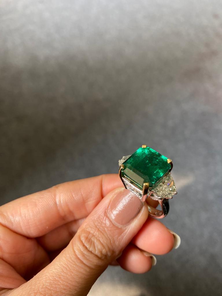 A statement three stone engagement ring, with a toip quality 12.17 carat transparent natural Zambian Emerald centre stone and 2 carat-each half-moon side stone diamonds. The emerald is of great lustre and has an ideal colour with very few minor