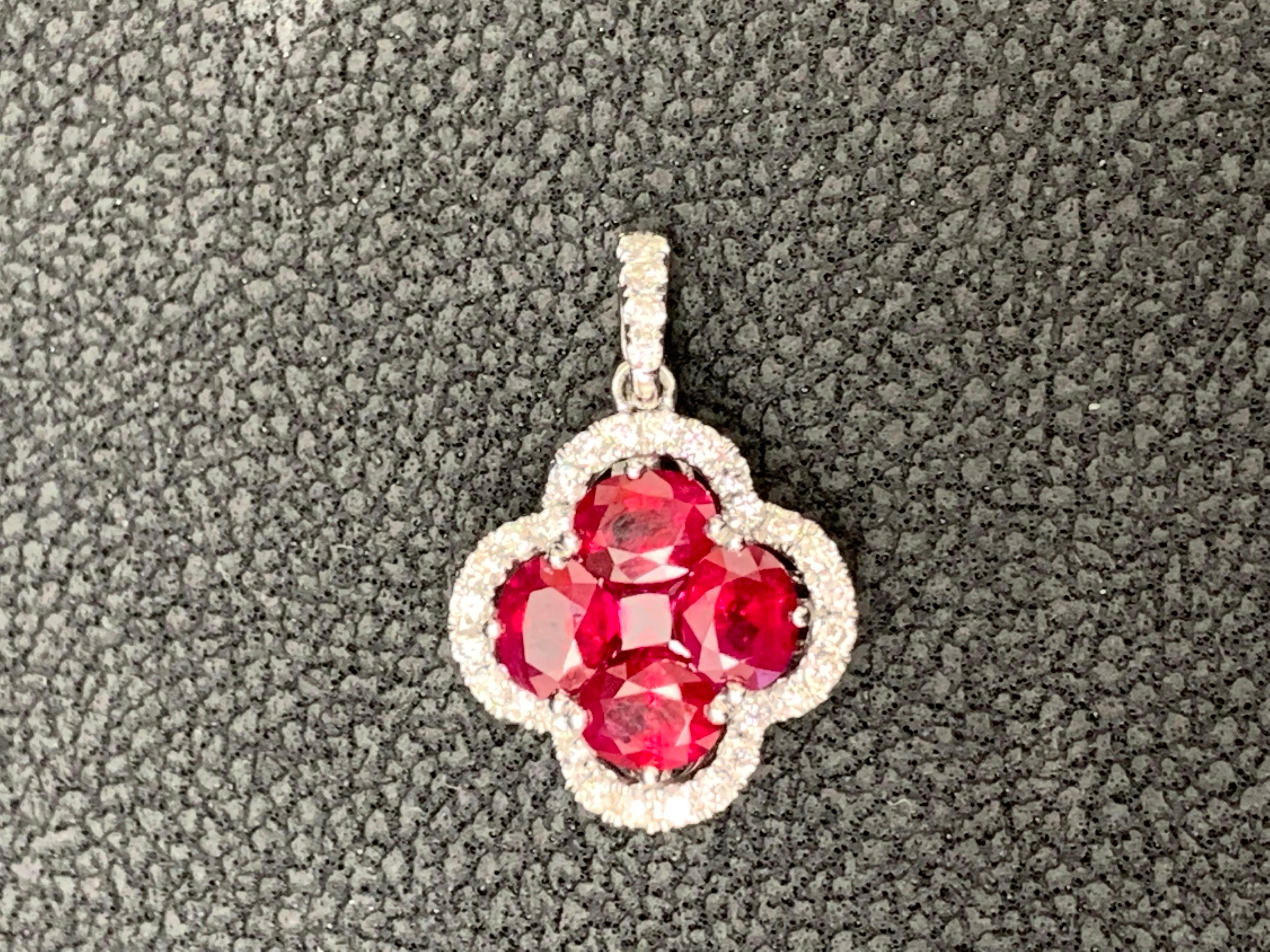 Showcasing flower design pendant with 4 oval shape Rubies weighing 1.22 carats total and 1 round shape Ruby weighing 0.13 carat, accented by a row of 33 round brilliant diamonds. Diamonds weigh 0.25 carats total. Set in a polished 18K white gold