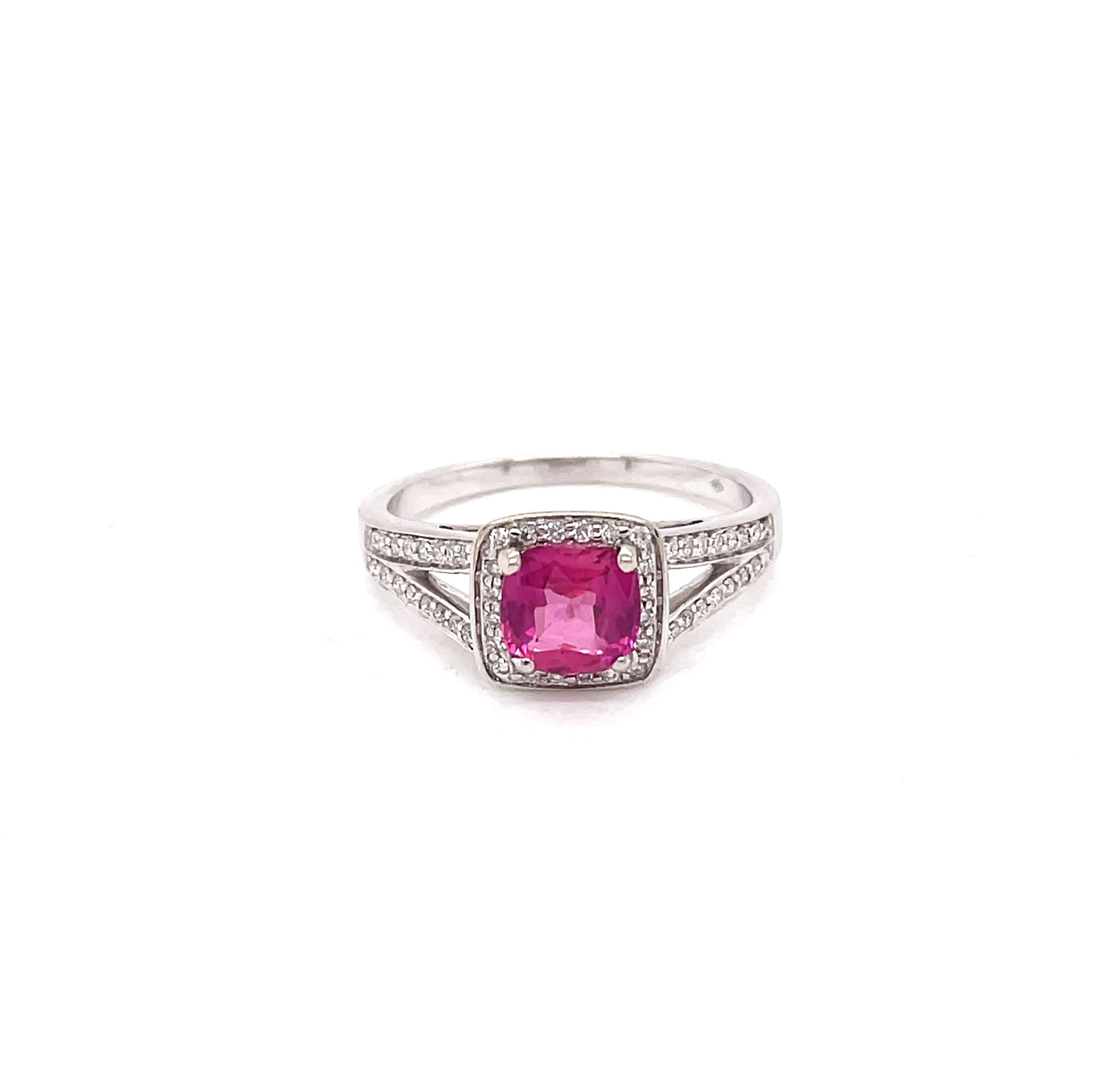 This stunning engagement ring features a vibrant cushion shaped pink sapphire weighing 1.22ct mounted in a four claw, open back setting. The gorgeous gemstone is surrounded by a halo of round brilliant cut diamonds mounted atop a diamond set split