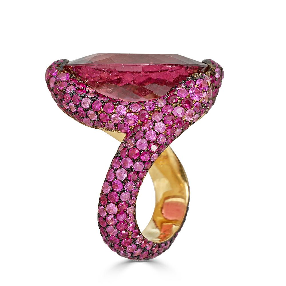 A beautiful 12.25 carat Rubellite Tourmaline ring set in handcrafted 18k Rose gold with approximately 6.2 carats of pave set pink sapphires. This ring is a freeform shape complimenting the Magenta Color Oval Cut Rubellite Tourmaline. The ring is
