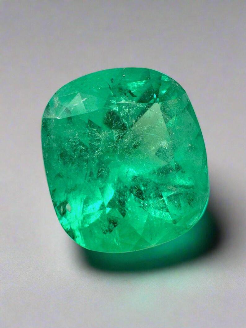 Stone: Emerald
Weight: 12.27-carats
Shape: Cushion Cut
Clarity: Transparent
Luster: Very Good
Color: Yellowish Green
Measurements: 15.24mm x 13.93mm x 10.56mm
Geographic Origin: Colombia
Treatment: Natural, Oiling

Comments: Due to their growth