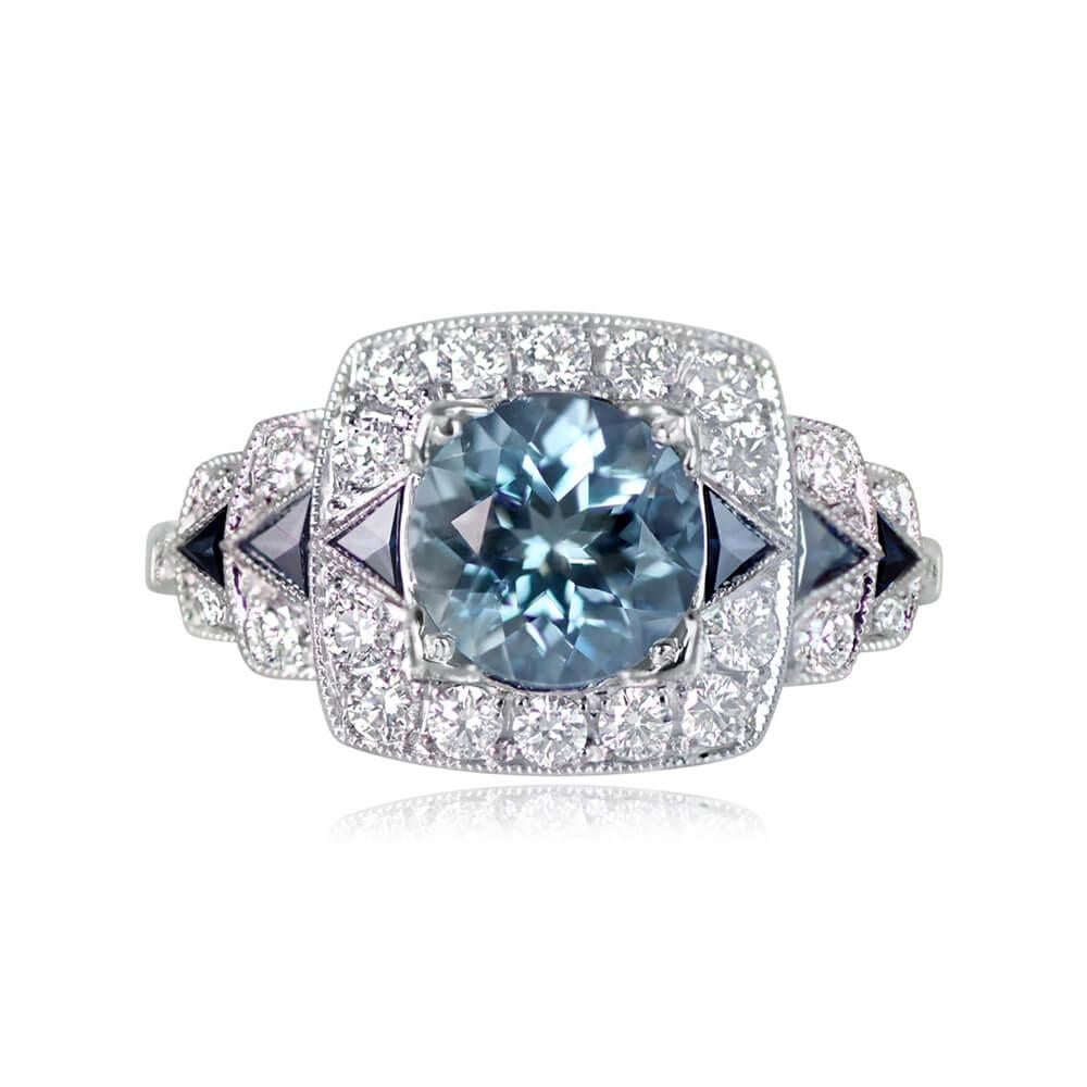 A stunning geometric gemstone ring with a 1.22-carat round cut aquamarine at its center, flanked by triangular French-cut sapphires on the sides and encircled by round brilliant cut diamonds. The total diamond weight is around 0.45 carats,