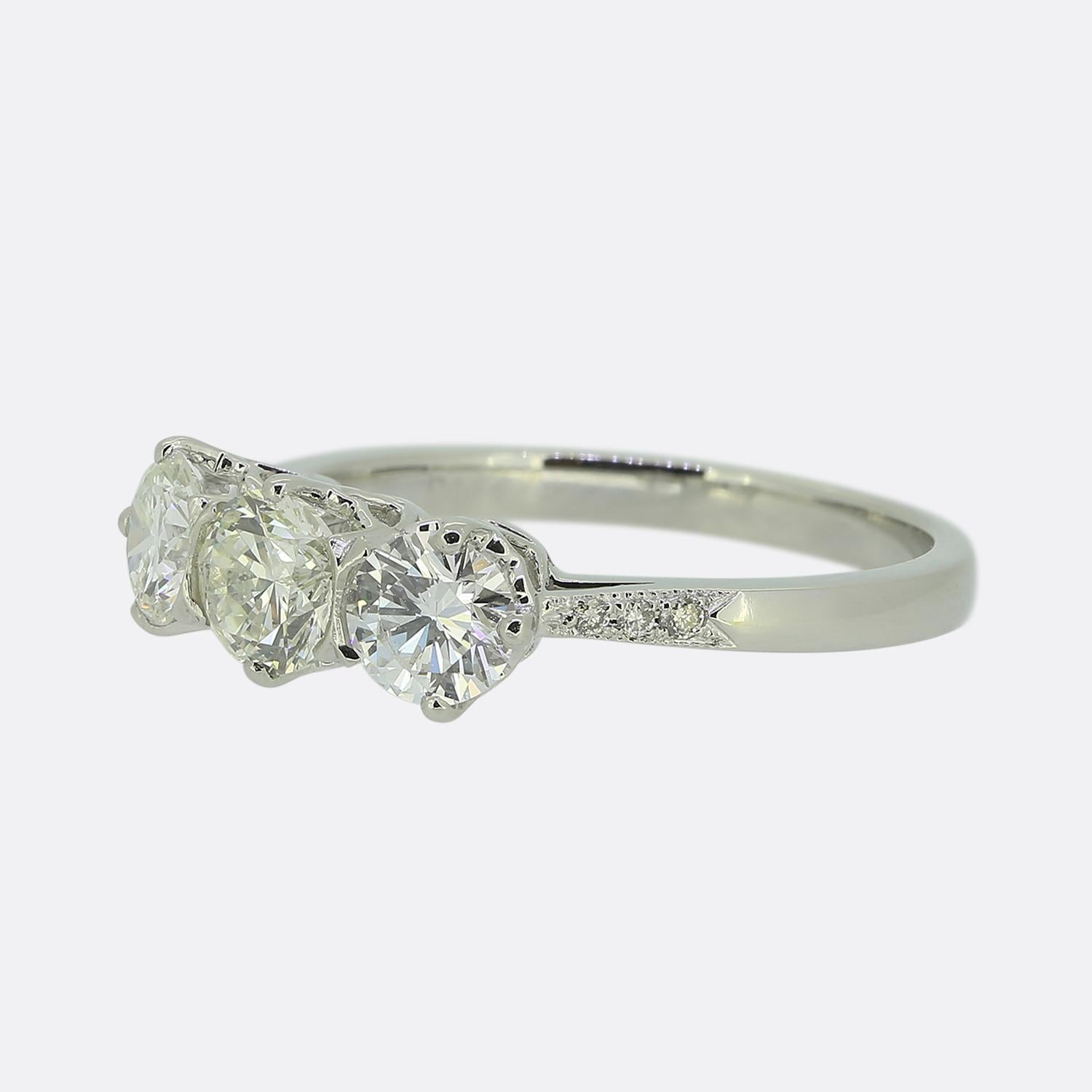 Ecco un affascinante anello con tre pietre e diamanti. Realizzato in platino, questo pezzo presenta tre diamanti rotondi taglio brillante, ognuno dei quali è stato incastonato singolarmente in una formazione collettiva a linea singola lungo il viso.