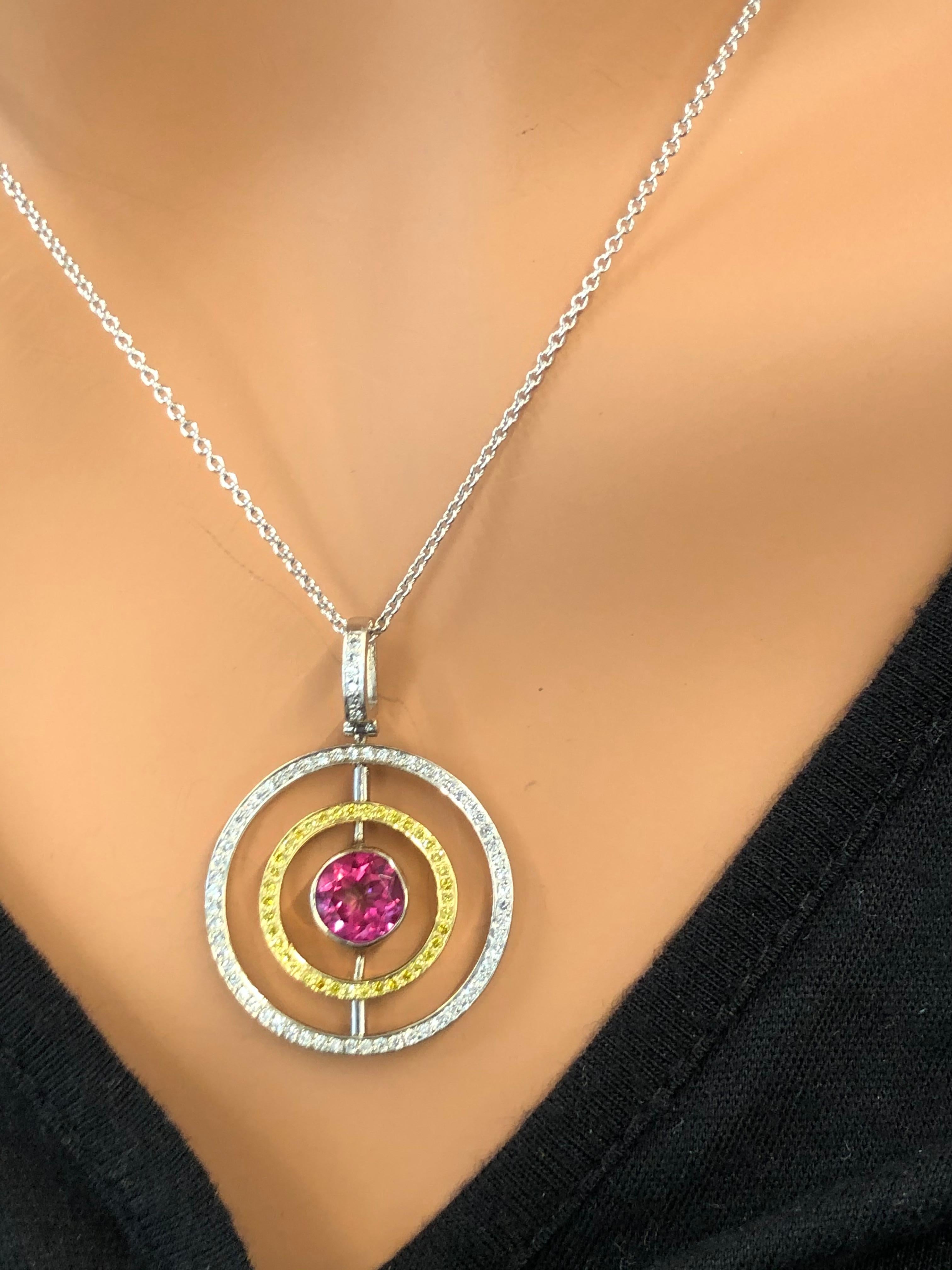 Designed in 18 karat two-tone gold, this modern eternity concentric circle pendant features a round brilliant cut raspberry pink tourmaline bezel set in the center. A total of 0.33 carat round brilliant white diamonds, 0.19 natural yellow diamonds,