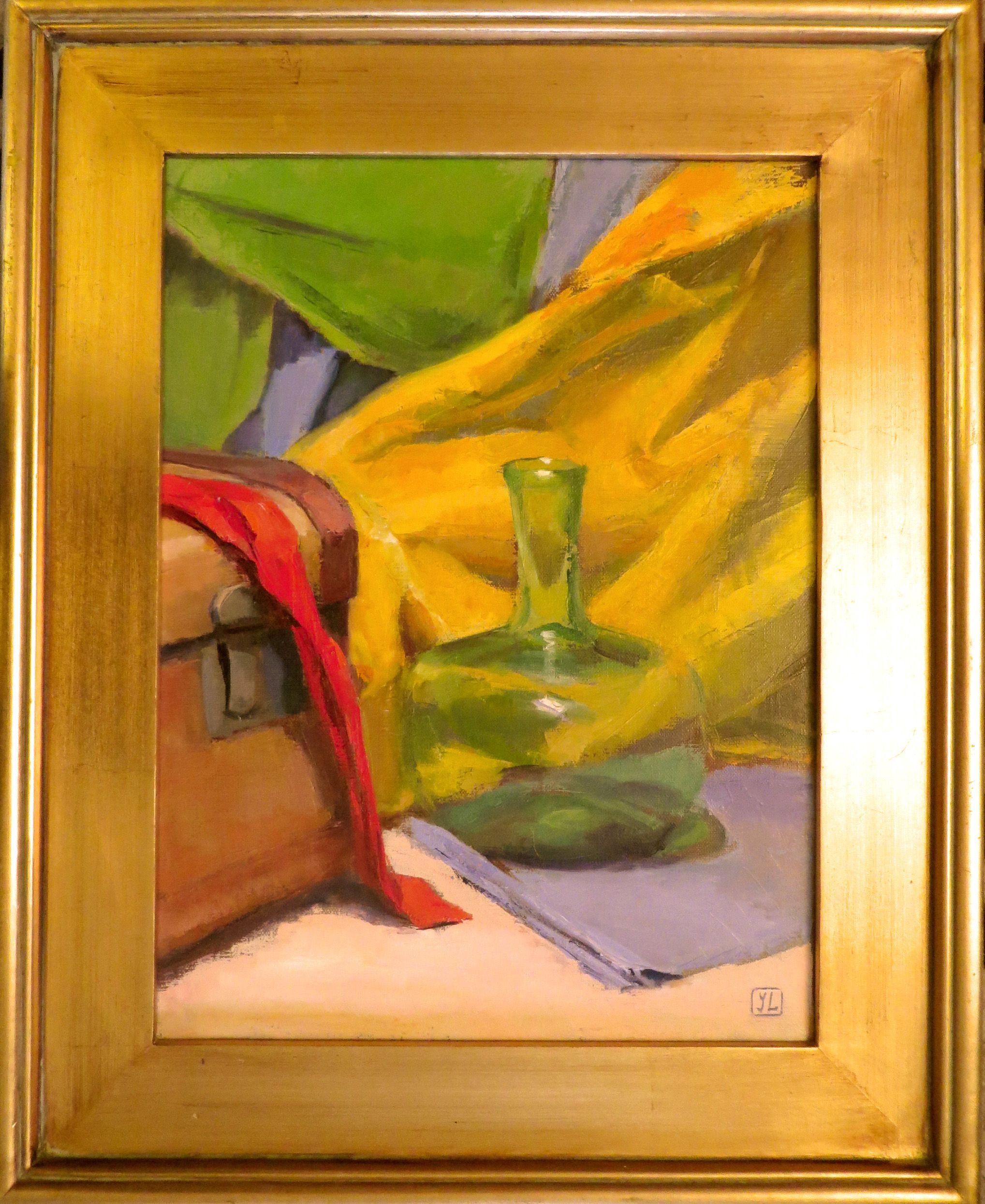 A green transparent bottle is sitting next to a leather suitcase.  This couple is surrounded by colorful fabrics - yellow, blue, green and red.  The whole composition of 'Green Bottle' is suffused in strong light which helps to emphasize the