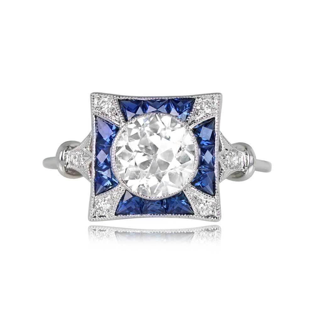 A captivating ring showcases a striking old European cut diamond, bezel-set within a charming sapphire and diamond mounting. The center diamond, 1.23 carats, dazzles with J color and SI1 clarity. French-cut calibre sapphires encircle the center,