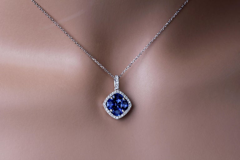 This pendant features a rounded square cluster of four oval cut and one princess cut vivid blue sapphires (total weight 1.24 carats), surrounded by a halo of round white diamonds, which also extend up the bail (total diamond weight 0.13