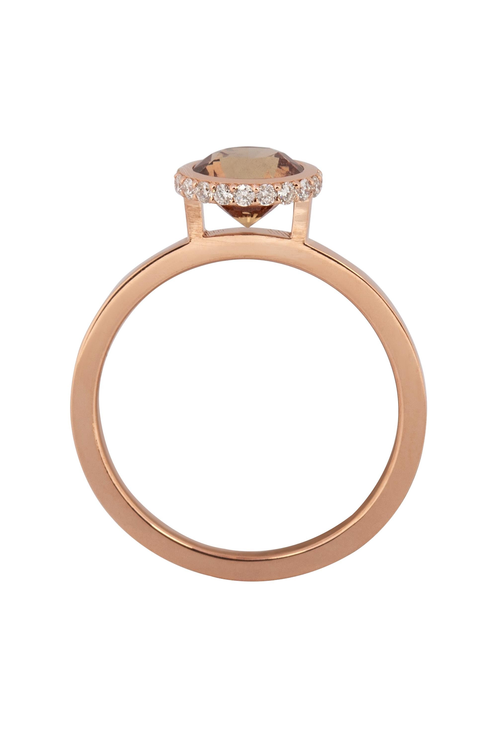 A strikingly modern solitaire ring featuring a round warm brownish orange sapphire, weighing approximately 1.25 carats, adroitly set in a custom made bezel frame edged in sparkling round brilliant diamonds weighing approximately .25 carats. Crafted