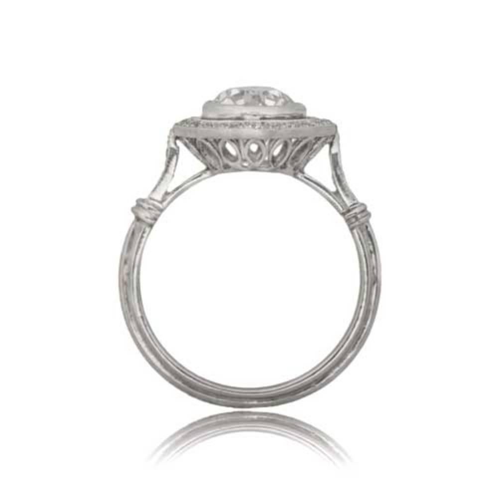 An enchanting engagement ring features an old European cut diamond, elegantly bezel-set in a finely crafted platinum mounting. The ring is adorned with a diamond halo set in bezels, complemented by three diamonds on each shoulder. The center