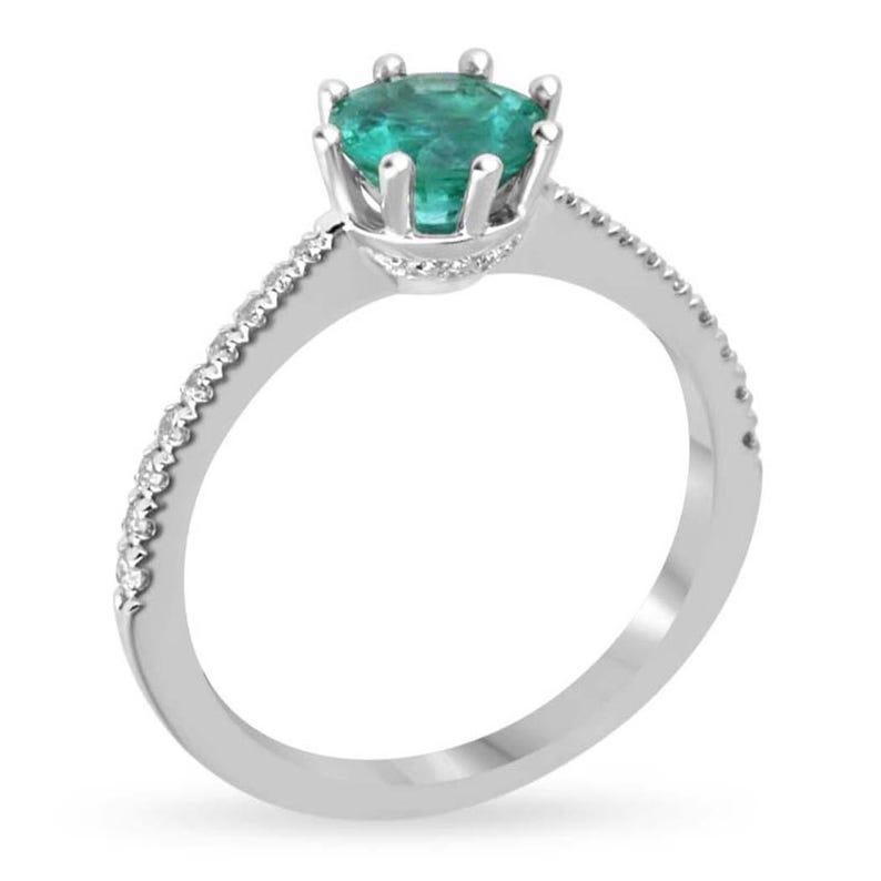 This exquisite emerald and diamond solitaire ring showcases a mesmerizing round-cut emerald in a bluish-green hue, set securely in an elegant eight-prong setting. The pinched shank is beautifully accented with round-cut diamonds, adding a touch of