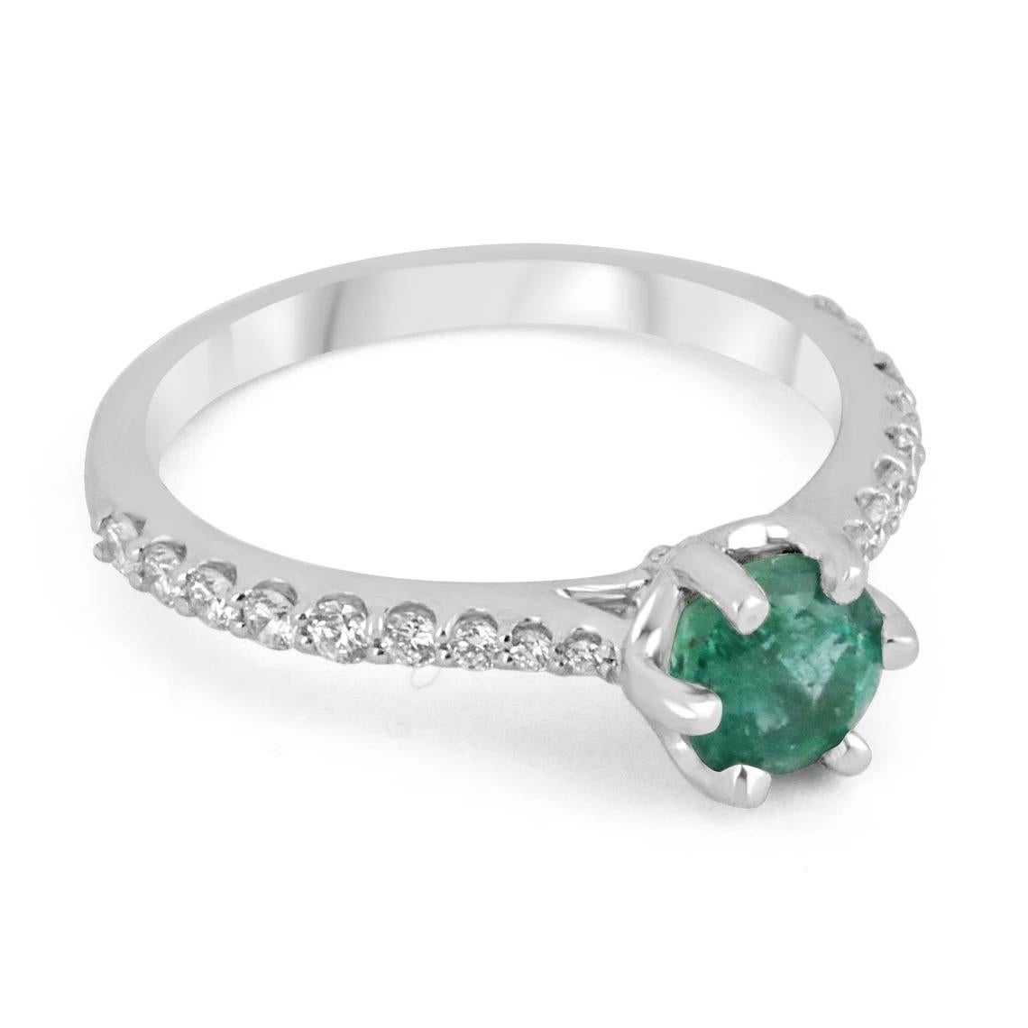 Elegantly displayed is a natural emerald and diamond engagement ring. The center stone carries a full carat, of natural round cut Zambian emerald with impressive qualities; vivid medium-dark bluish-green color and excellent clarity. This