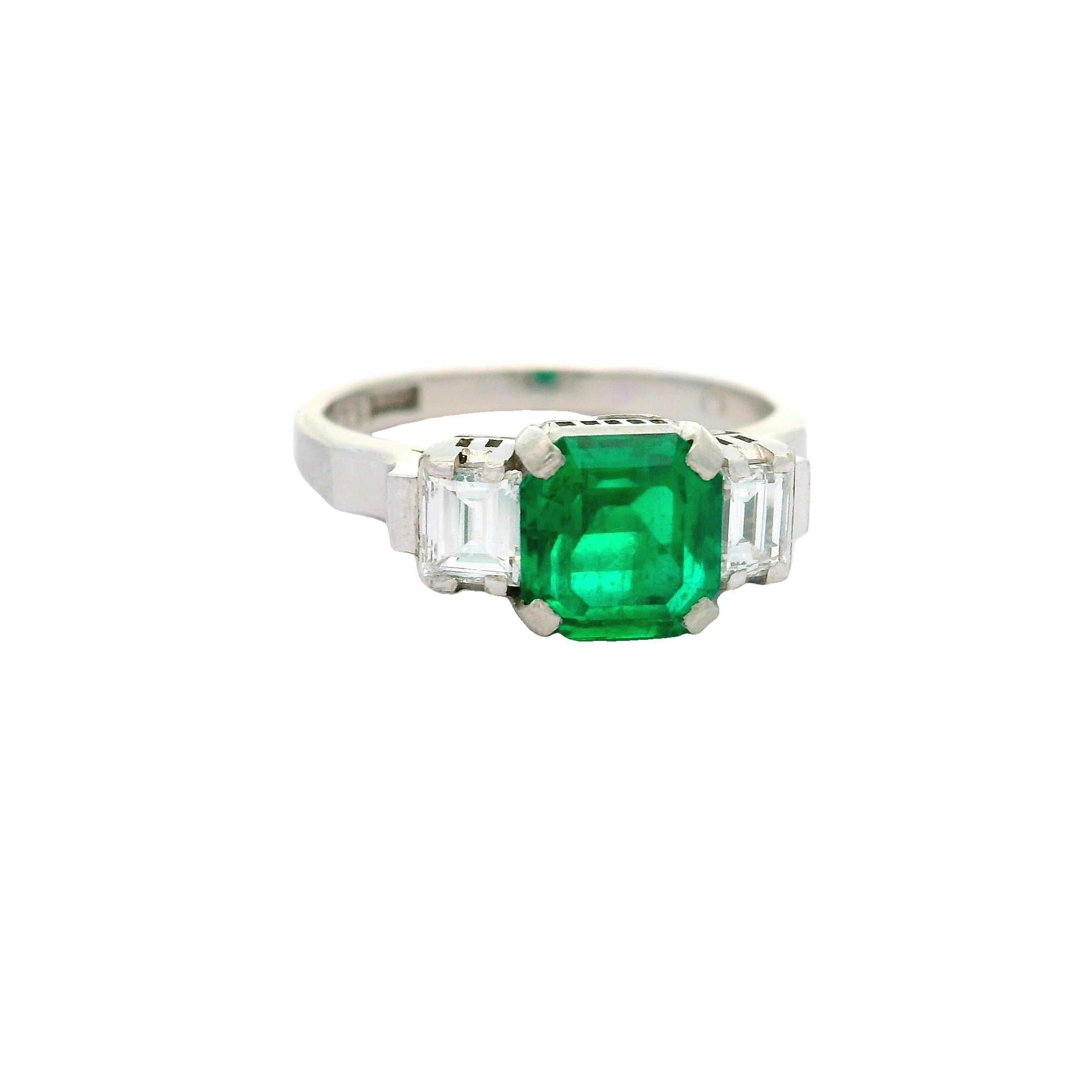 A striking emerald-cut emerald, weighing 1.26 carats, commands attention at the center of this classic three-stone ring. The emerald has an amazing intense green color mainly found in only older antique Colombian stones known in the trade as