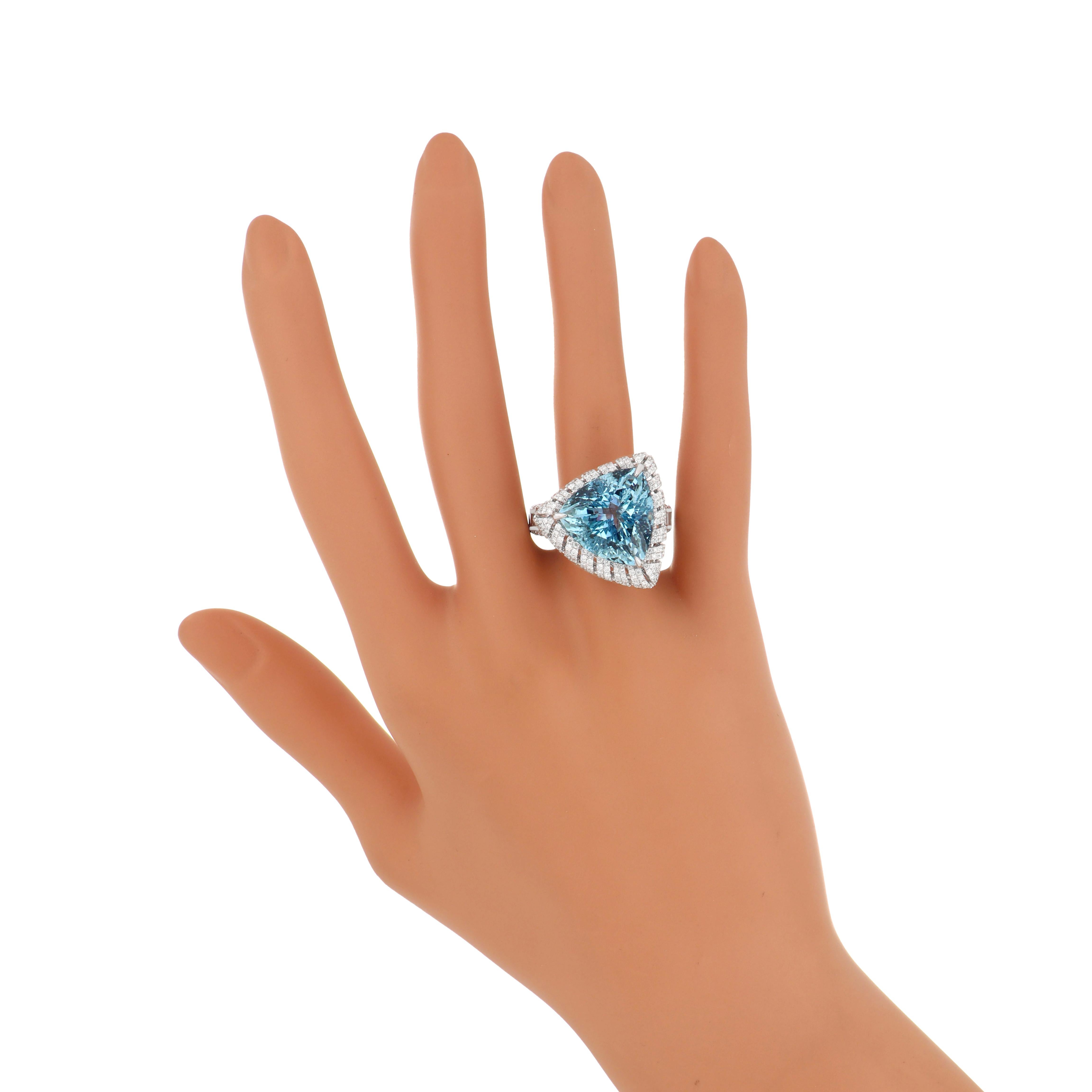 Step into the world of unparalleled luxury with our impeccably crafted 18 karat White Gold Ring. Gracing its center is a majestic 12.6 carat (approx.) Trillion Shape Aquamarine, radiating beauty and grace. Encircling this stunning gemstone is a halo