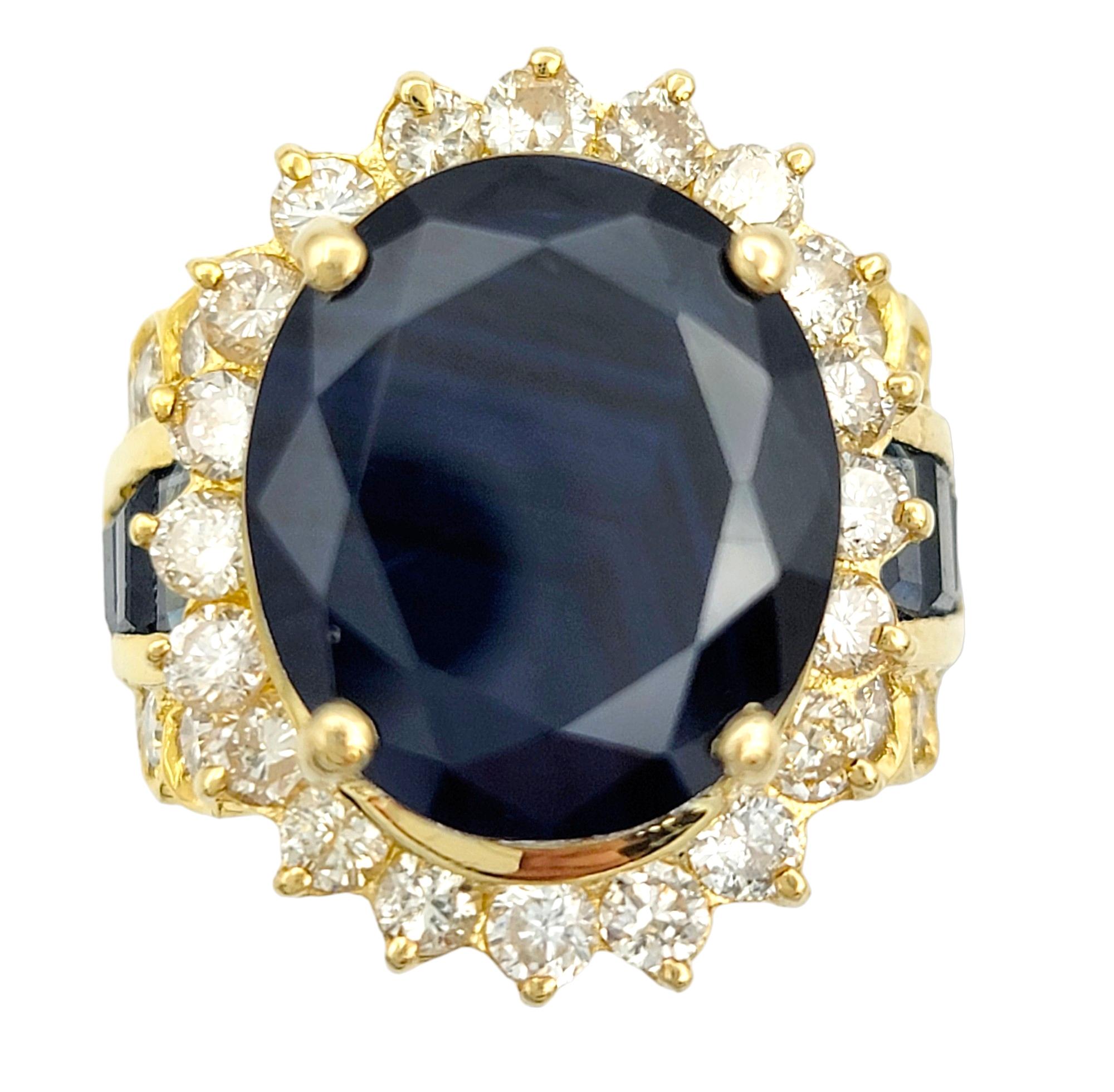Ring Size: 7 

This striking sapphire cocktail ring, set in sumptuous 18 karat yellow gold, is an opulent statement piece. At its heart lies a large, mesmerizing blue oval sapphire, exuding a rich and captivating hue. A halo of brilliant round