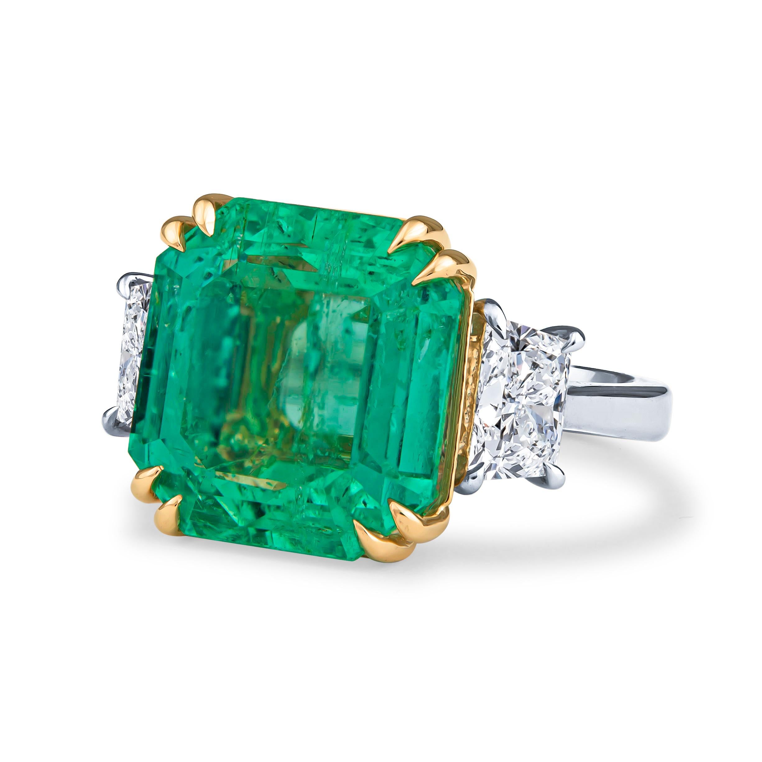 This jaw-dropping 12.65ct natural Colombian emerald is a square step cut, GIA certified gem (GIA 2201417901, F2 clarity). It is set in a platinum ring with two 0.88ct total weight trapezoid diamonds and an 18kt yellow gold double prong basket