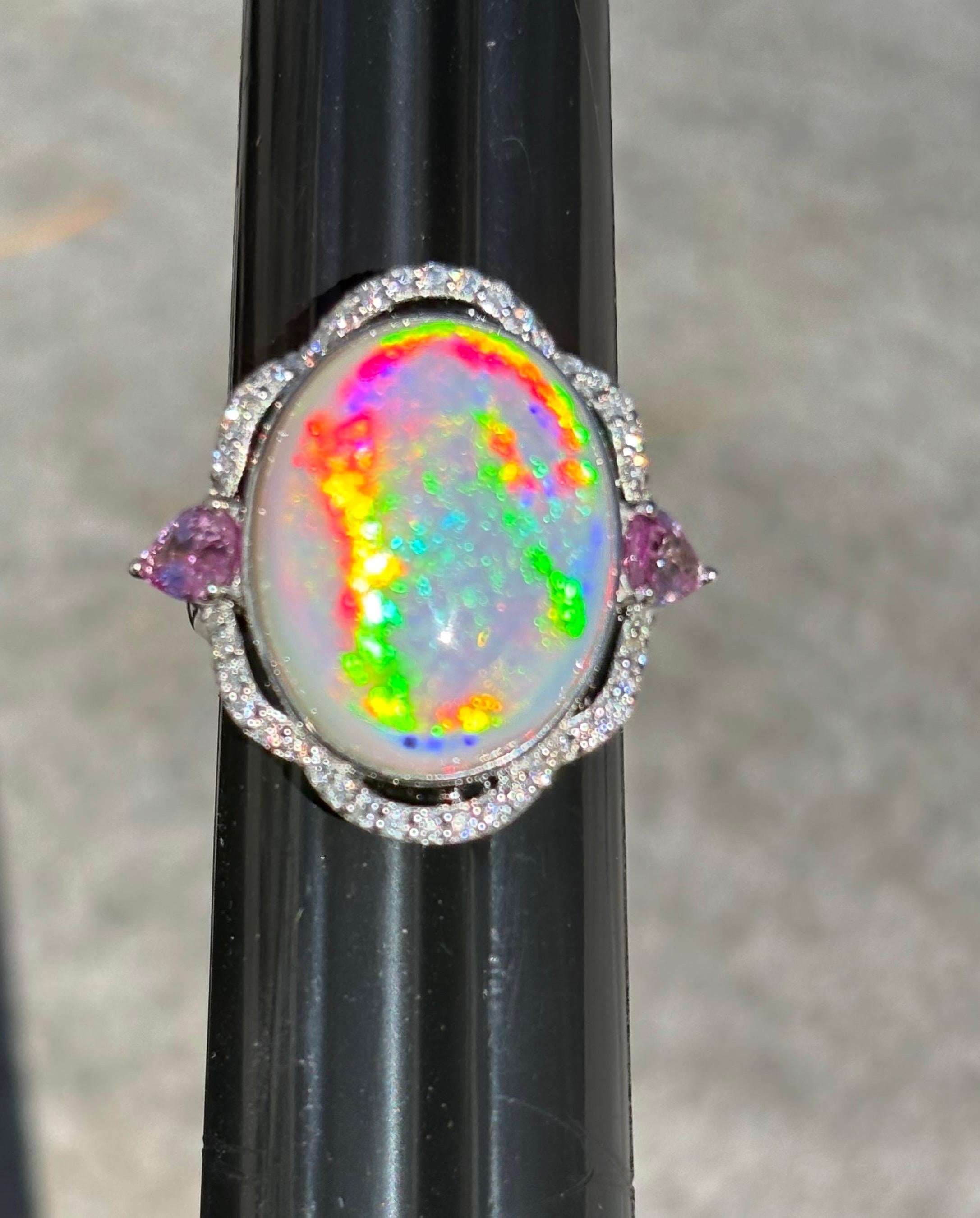 This exquisite ring boasts a 12.69-carat oval opal with remarkable fire. The centerpiece is flanked by two 0.92-carat pear-cut pink sapphires set to the east and west, while a scalloped halo of diamonds totaling 0.35 carats accentuates the design.