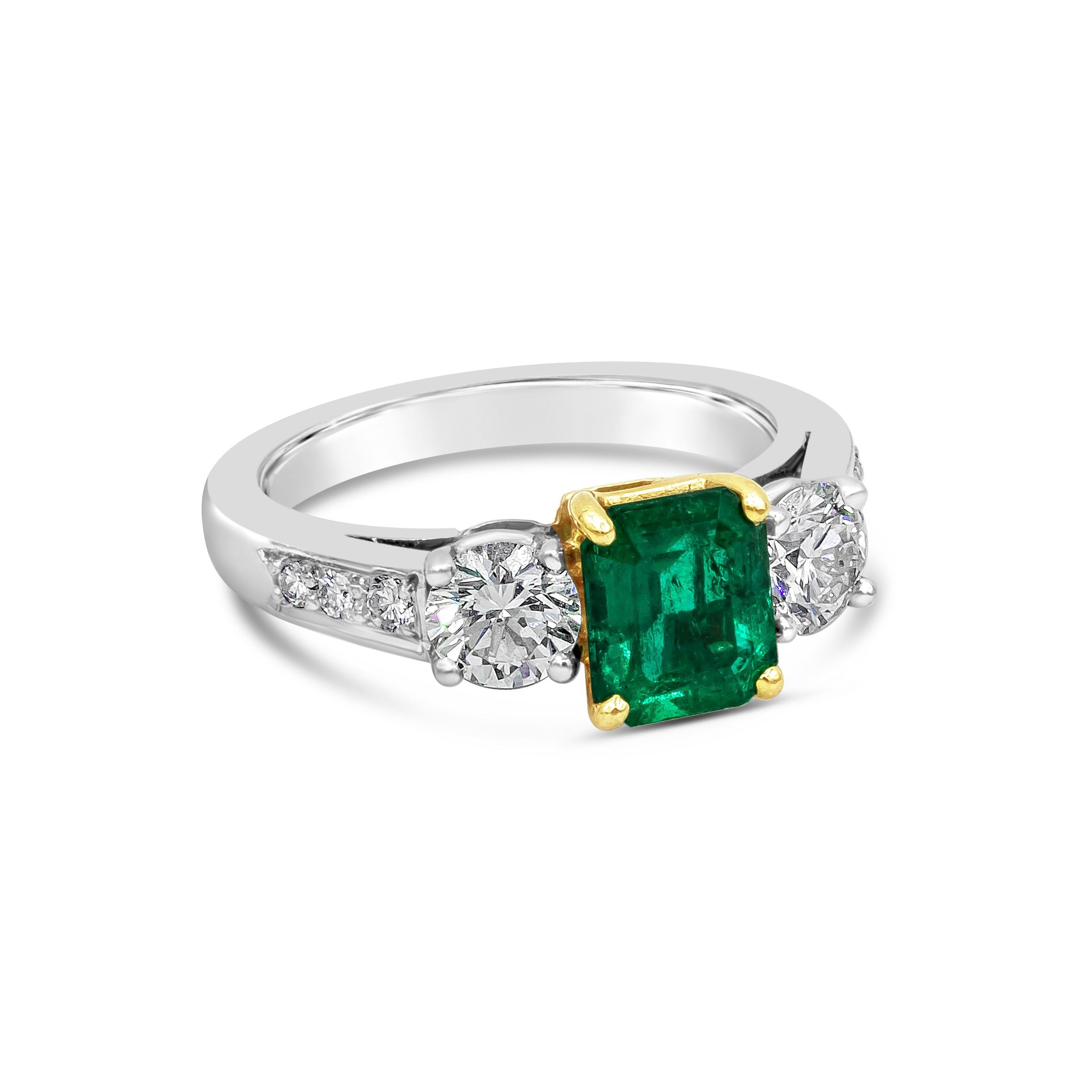 A color-rich three stone engagement ring showcasing a 1.27 carats green emerald, set in a classic four prong setting. Flanked by a round brilliant diamond on each side and set in a polished platinum band accented with round brilliant diamonds.