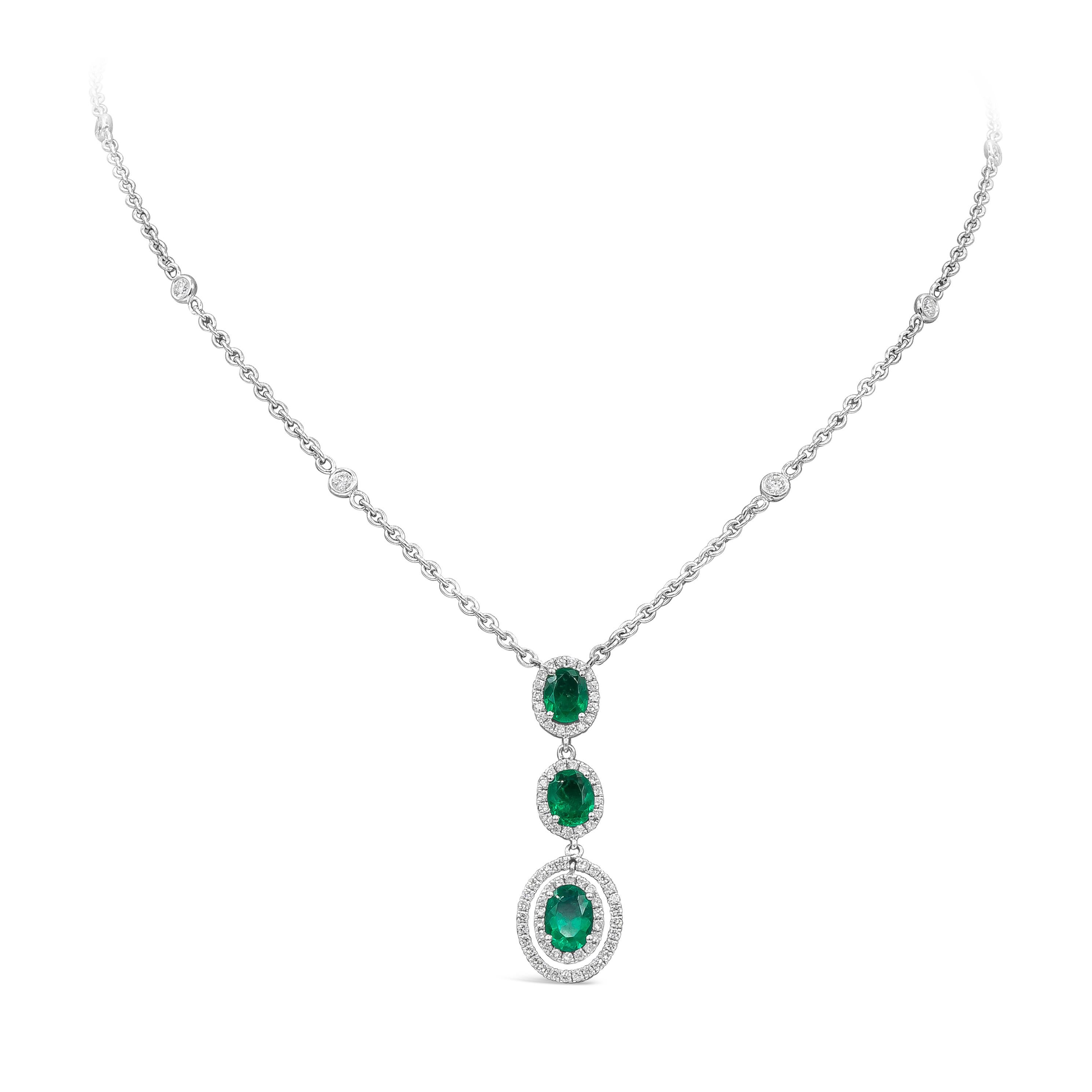 A gorgeous drop pendant necklace showcasing three oval cut emeralds, each surrounded by a row of round brilliant diamonds. Suspended on an 18 inch white gold chain. Green emeralds weigh 1.28 carats total; diamonds weigh 0.70 carats total. Finely