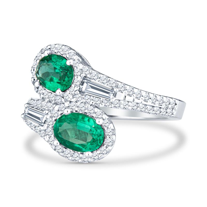 This unique bypass ring features 1.28 carat total weight in oval cut natural emeralds accented by 0.88 carat total weight in baguette and round diamonds set in 14 karat white gold. It is a size 6.5 but can be resized upon request.