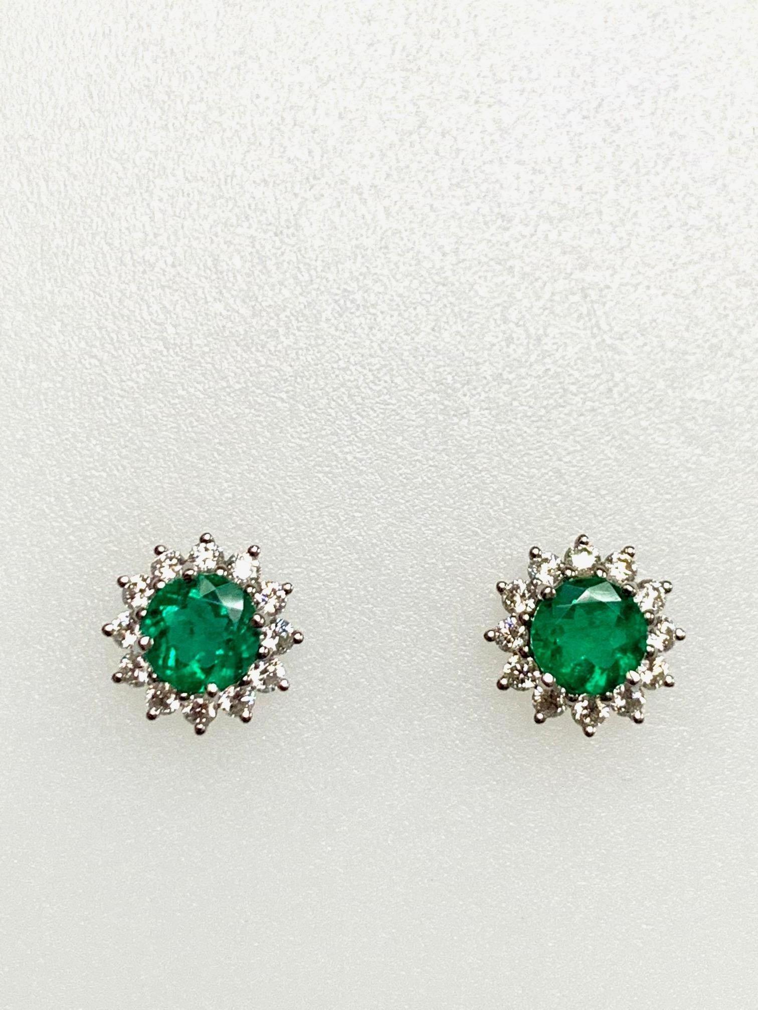 1.29 Carat zambian emerald round shape set in classic 18k white gold earrings with 0.62 carat diamonds , g-h si1, around it .