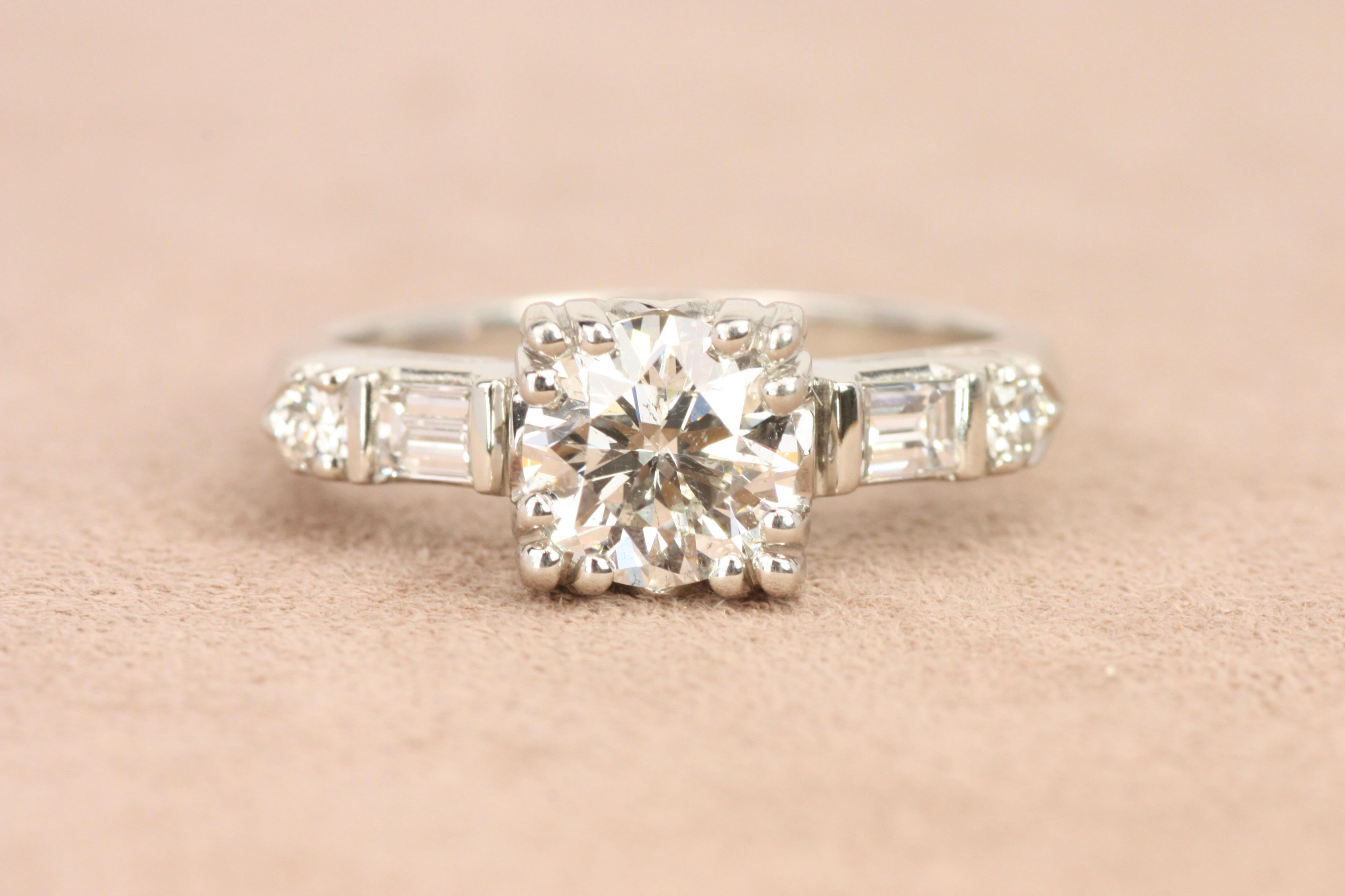 Featuring a unique blend of round and baguette diamonds, this 1950s-inspired platinum engagement ring offers balanced symmetry and classic beauty. The 1.02ct round brilliant cut diamond at center is framed by baguette and round side diamonds, with a