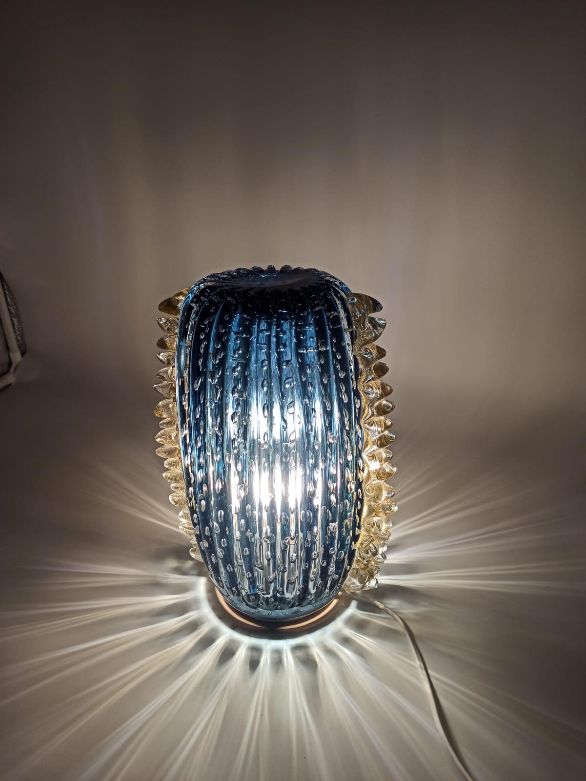 Presentiamo la nostra esclusiva lampada da tavolo, alta 35 cm e realizzata con maestria in vetro artistico di Murano. Questo affascinante pezzo è immerso in una vibrante tonalità turchese, caratterizzato da bolle ballotton sottoposte al vetro e