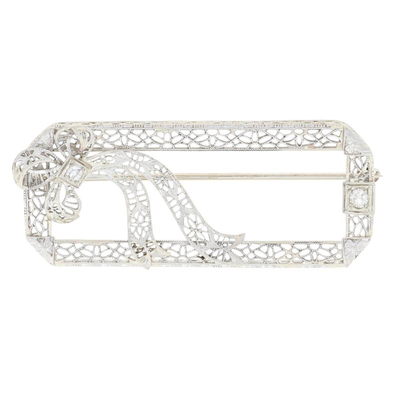 This exquisite Art Deco brooch would make a wonderful gift for someone who treasures jewelry from yesteryear. Dating from circa 1920s -1930s, the brooch features a filigreed frame adorned on one corner with a bow. A natural diamond accent shimmers