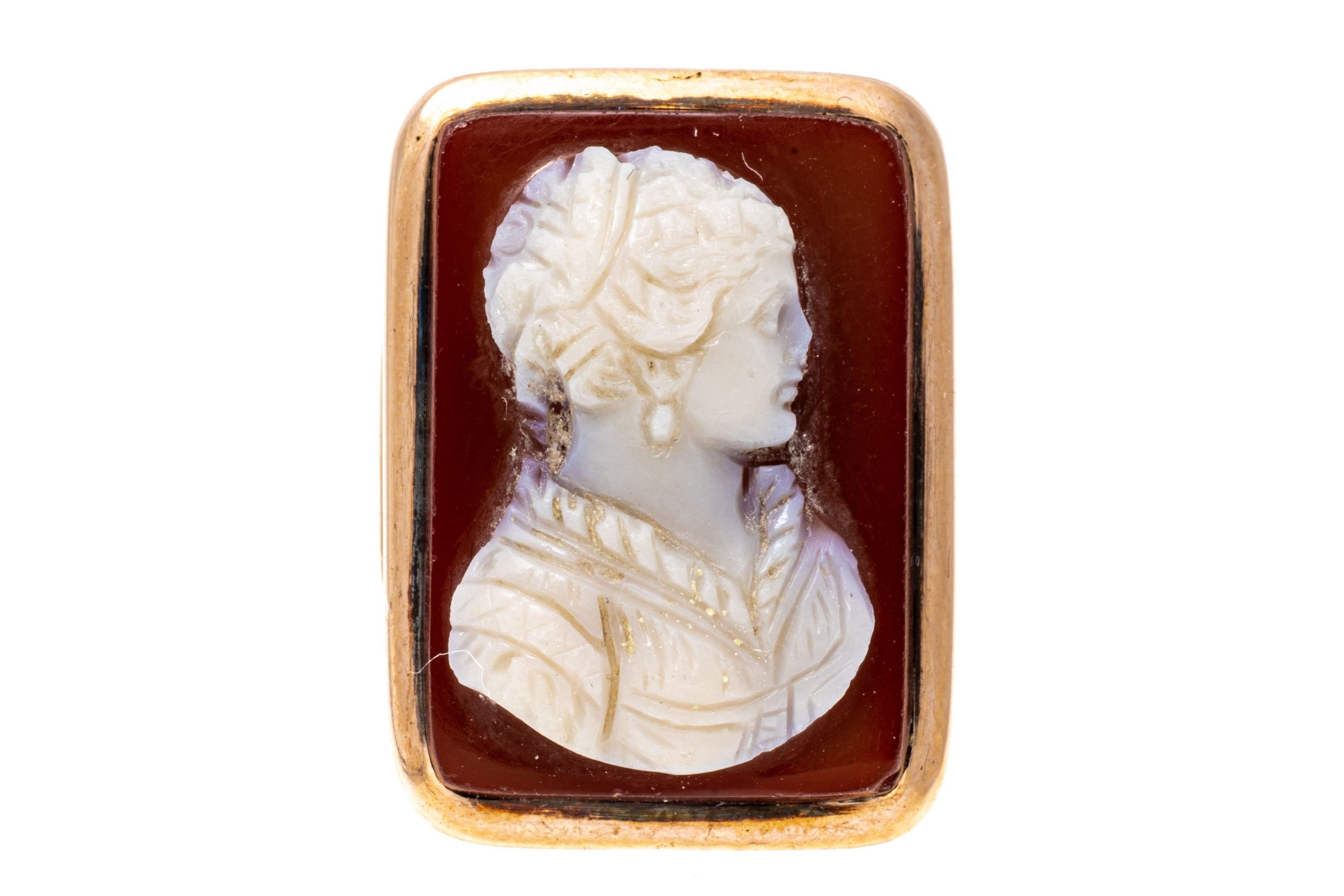 12k rose gold ring. This lovely antique rectangular cameo ring has an orange background with a creamy white foreground of a handsome profile bust, facing to the right, and decorated with a pendant earrings and intricate collar. The ring also has a