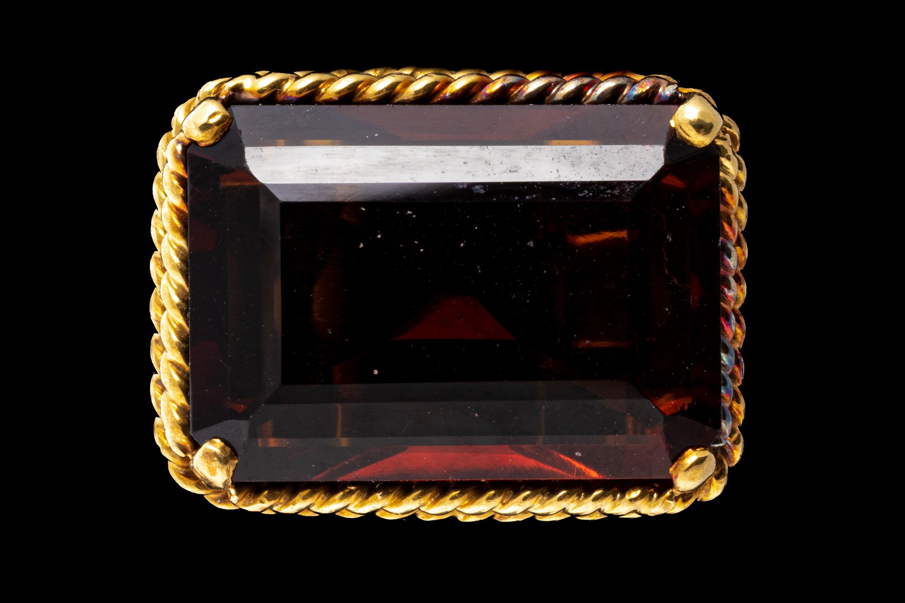 12k yellow gold ring. This striking ring is a horizontal profile, emerald cut, dark orange color citrine, approximately 9.43 CTS, prong set in a twisted wire setting, with split twisted wire shoulders and shank.
Marks: None, tests 12k
Dimensions: