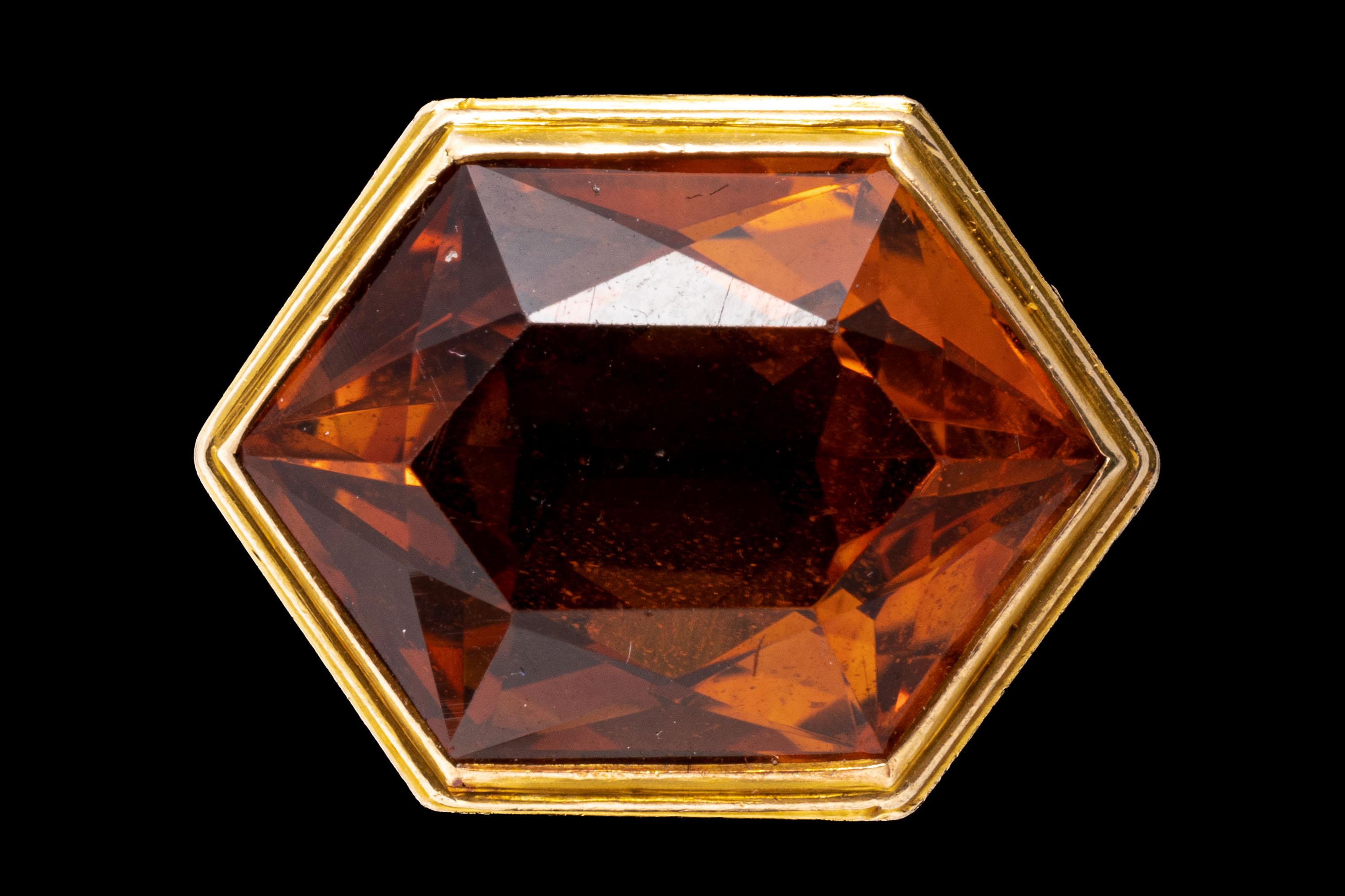 12k yellow gold ring. This wonderful ring features a center elongated hexagonal faceted, medium to dark orange color citrine, horizontally situated, and decorated with a grape and vine motif gallery and sides.
Marks: None, tests 12k
Dimensions: