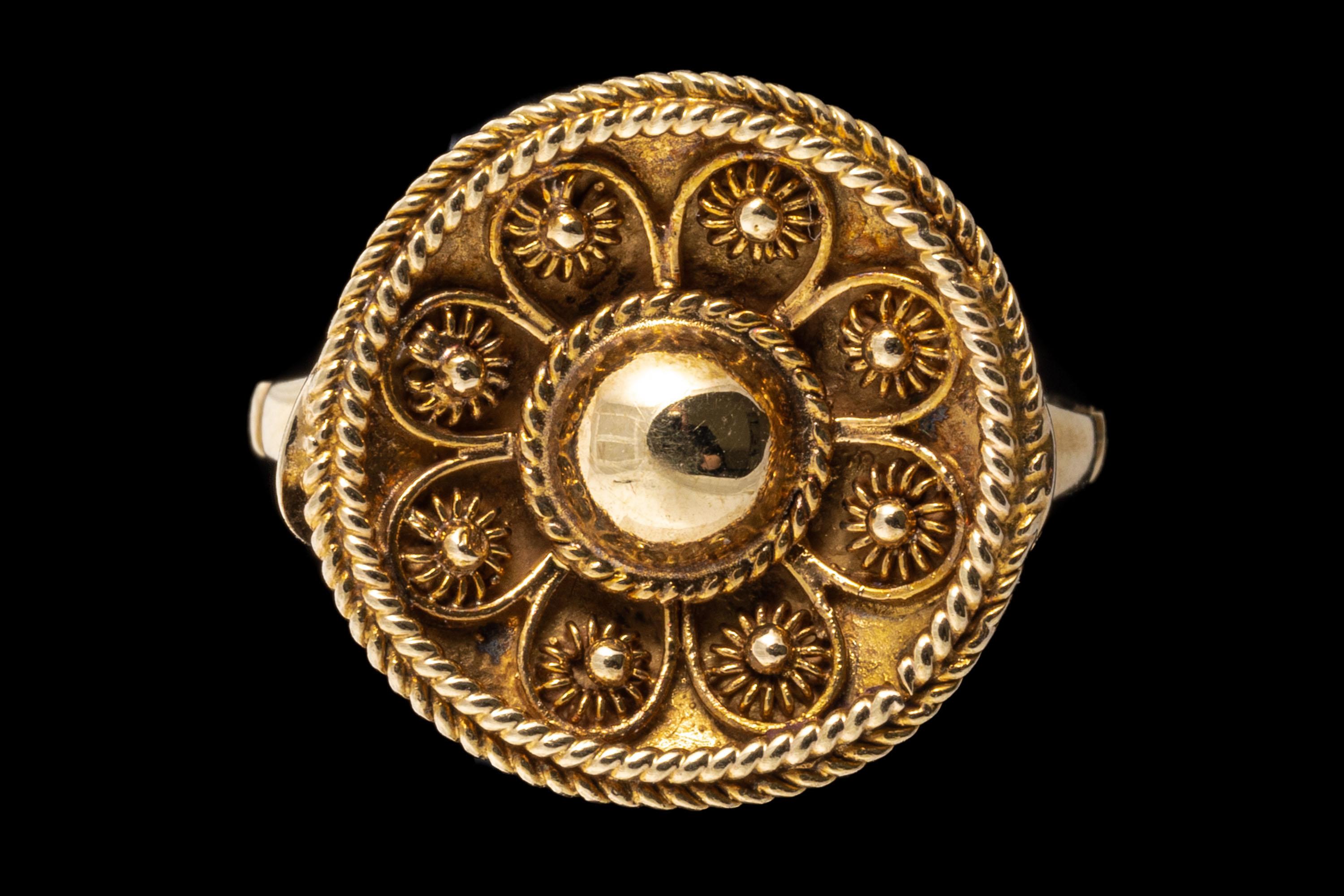 12k yellow gold ring. This pretty, ornate ring is a round profile top, with an Etruscan style patterning and a rope edged frame. The ring is finished with indented, concave shoulders.
Marks: None, tests 12k
Dimensions: 9/16