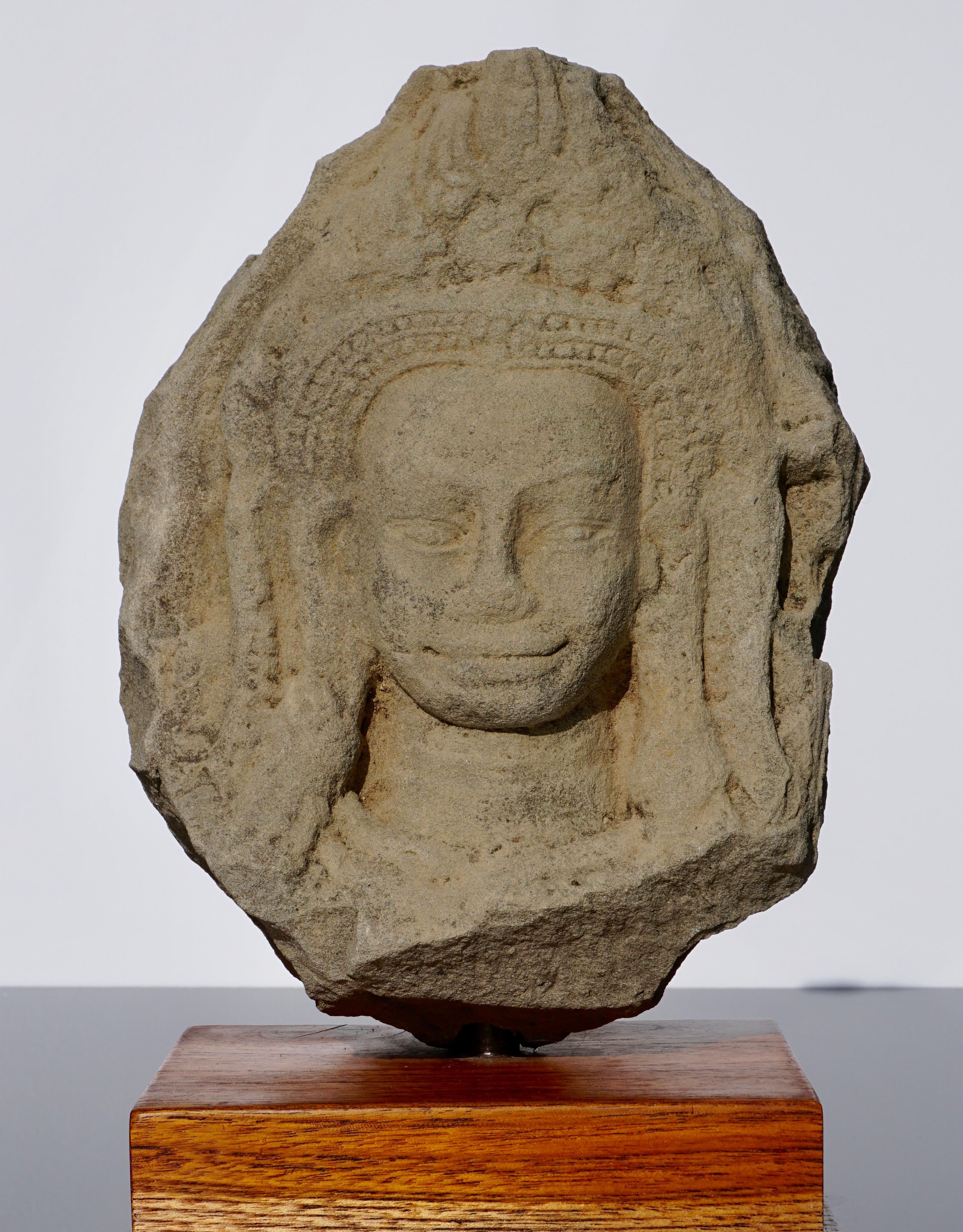 A large Cambodian Angkor Wat attributed sandstone head of an Apsara with an ornate flame crown. Mounted on a wood base, 12th century.

Measures: Height 11 x 9 inches
With stand 13.3 inches (34 cm)

Provenance: From a Canadian auction selling the