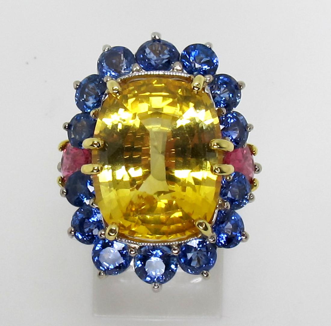 This platinum cocktail ring features an impressive 13.73 carat cushion-shaped yellow sapphire, set with blue sapphires and gorgeous pink tourmalines! The vibrant golden center gem sparkles like the sun with its rich golden hue and extraordinary