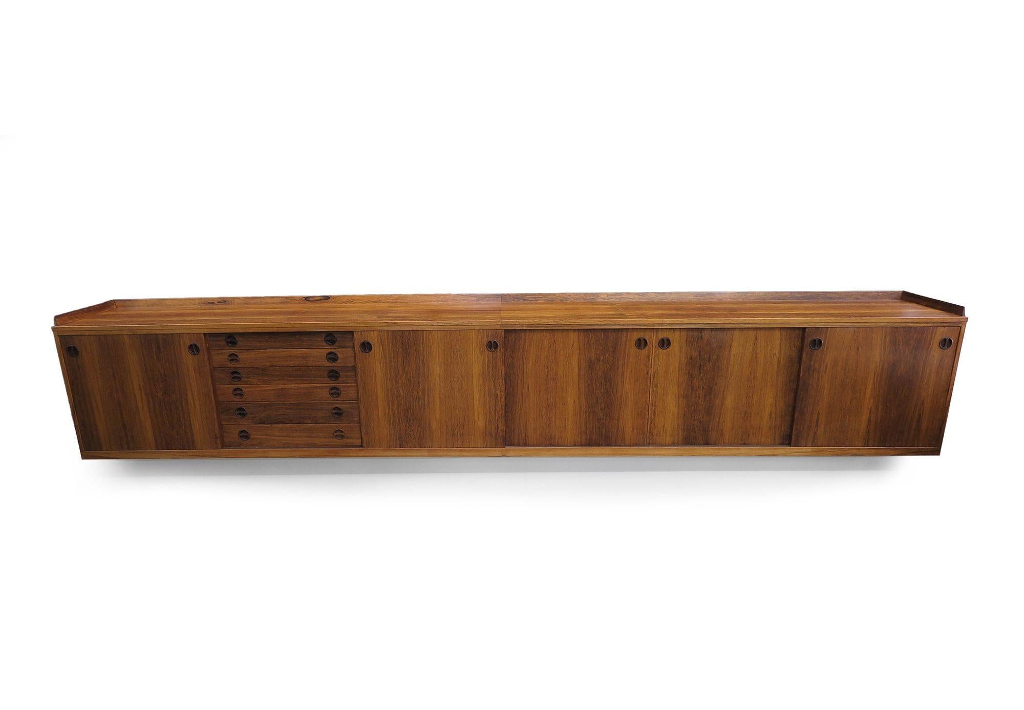 Impressive 1950s 13-foot wall-mount credenza with five sliding doors and six drawers, each adorned with carved recessed pulls. Crafted with meticulous attention to detail, it features railed trim, mitered corners, and dovetail joinery, showcasing