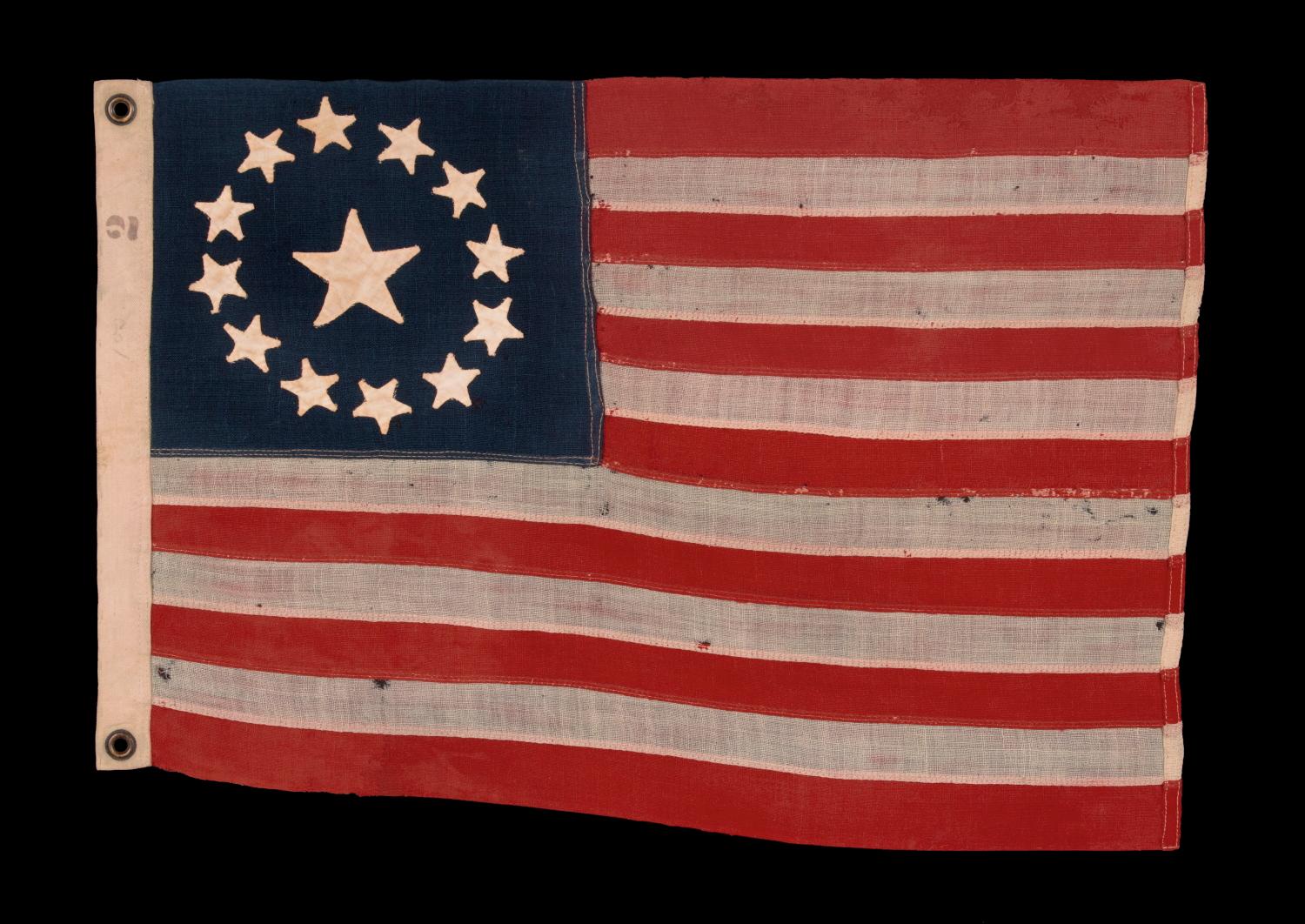 13 handgenähte Sterne in einer kreisförmigen Version des sogenannten 3. Maryland-Musters, mit einem besonders großen Stern in der Mitte, eine Flagge mit besonders kleinem Maßstab unter den Flaggen mit gestickter und genähter Konstruktion,