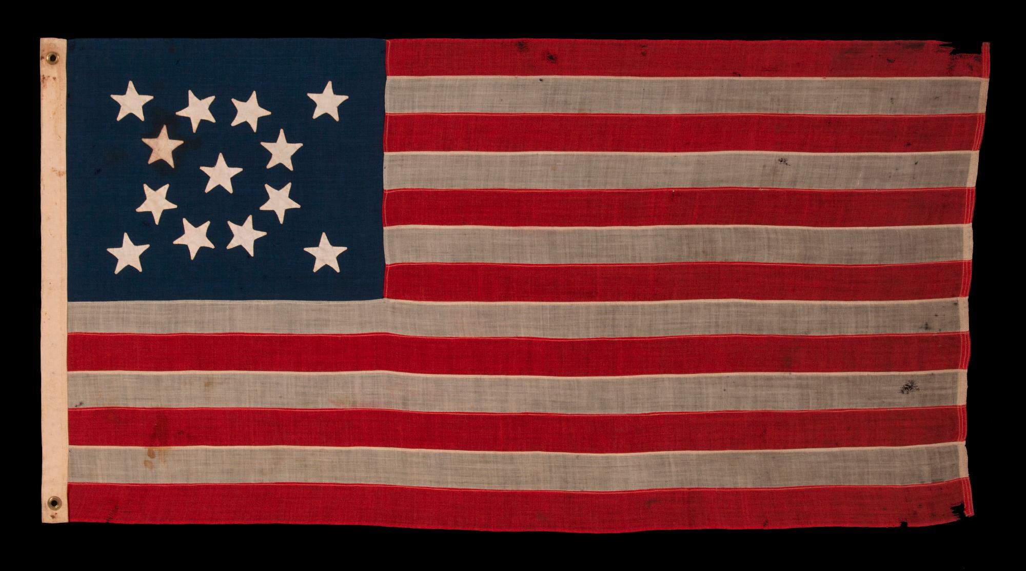 13 STAR ANTIQUE AMERICAN FLAG WITH A MEDALLION CONFIGURATION OF HAND-SEWN STARS AND A BEAUTIFUL, ELONGATED PROFILE, MADE IN THE ERA OF THE 1876 CENTENNIAL OF AMERICAN INDEPENDENCE, IN AN UNCOMMONLY SMALL SIZE AMONG ITS COUNTERPARTS OF THE PERIOD