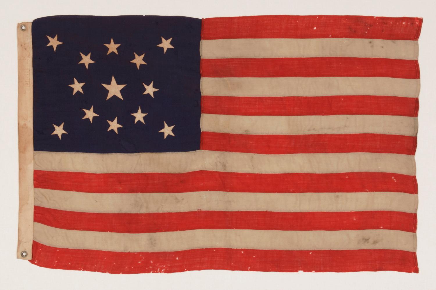 13 STARS IN A MEDALLION CONFIGURATION ON A SMALL-SCALE ANTIQUE AMERICAN FLAG OF THE 1895-1926 ERA:

13 star flag of the type made from roughly the last decade of the 19th century through the first quarter of the 20th. The stars are arranged in a